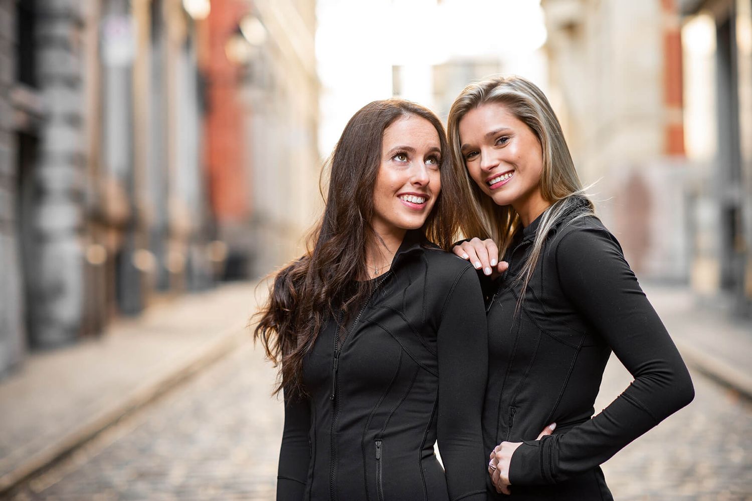 Two friends share candid moments during urban photoshoot in black outfits.