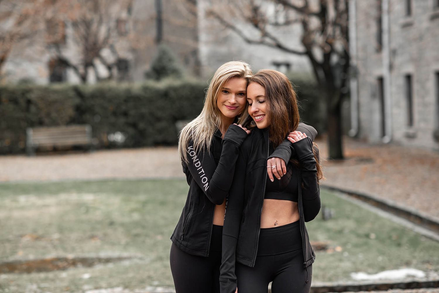 Two athletes in black workout gear pose together during outdoor fitness session.