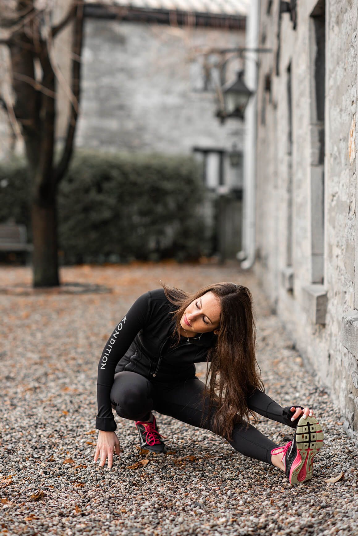 Fitness stretching routine demonstrated on gravel path beside stone architecture.