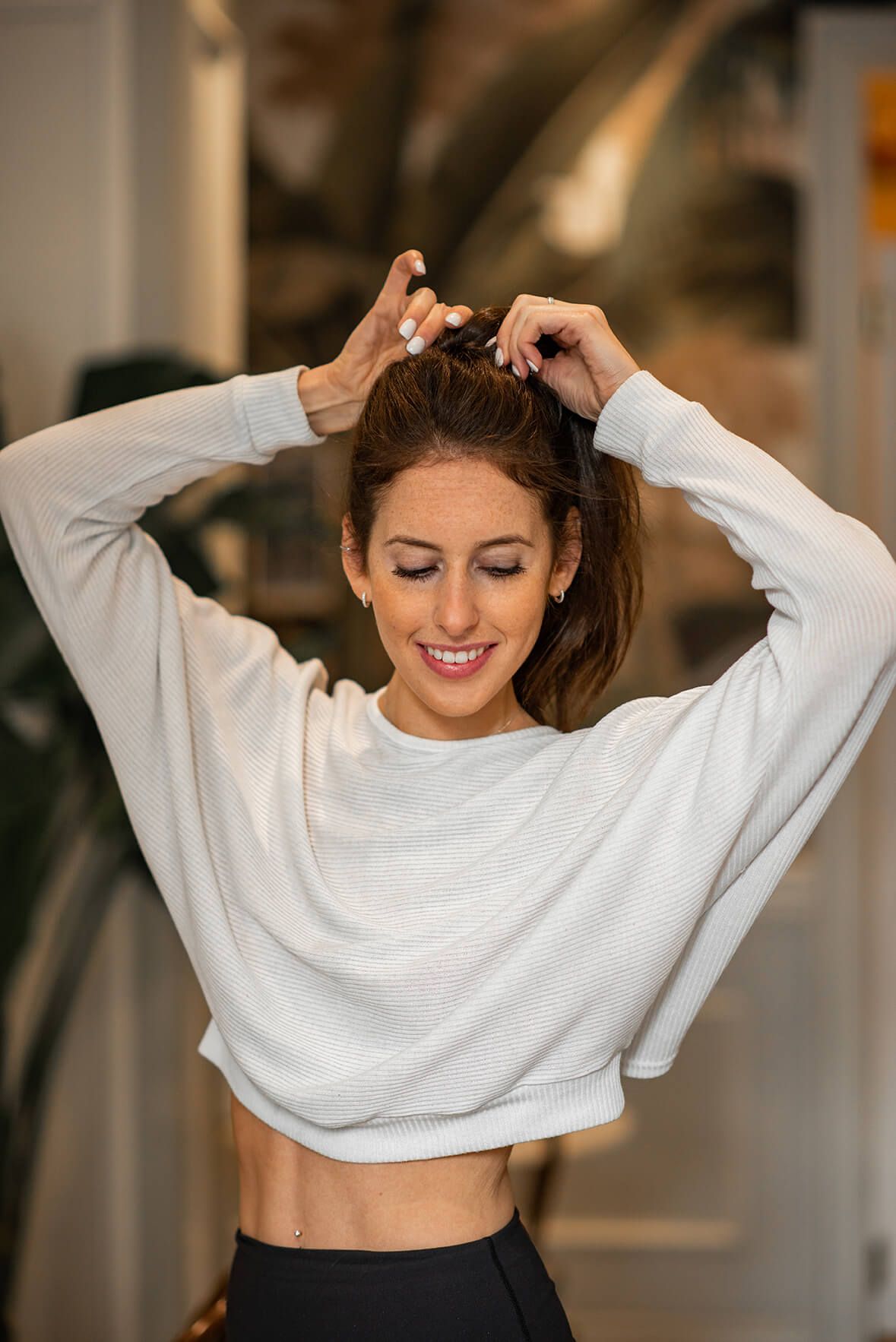 Joyful fitness portrait of someone in white cropped sweatshirt fixing their hair.