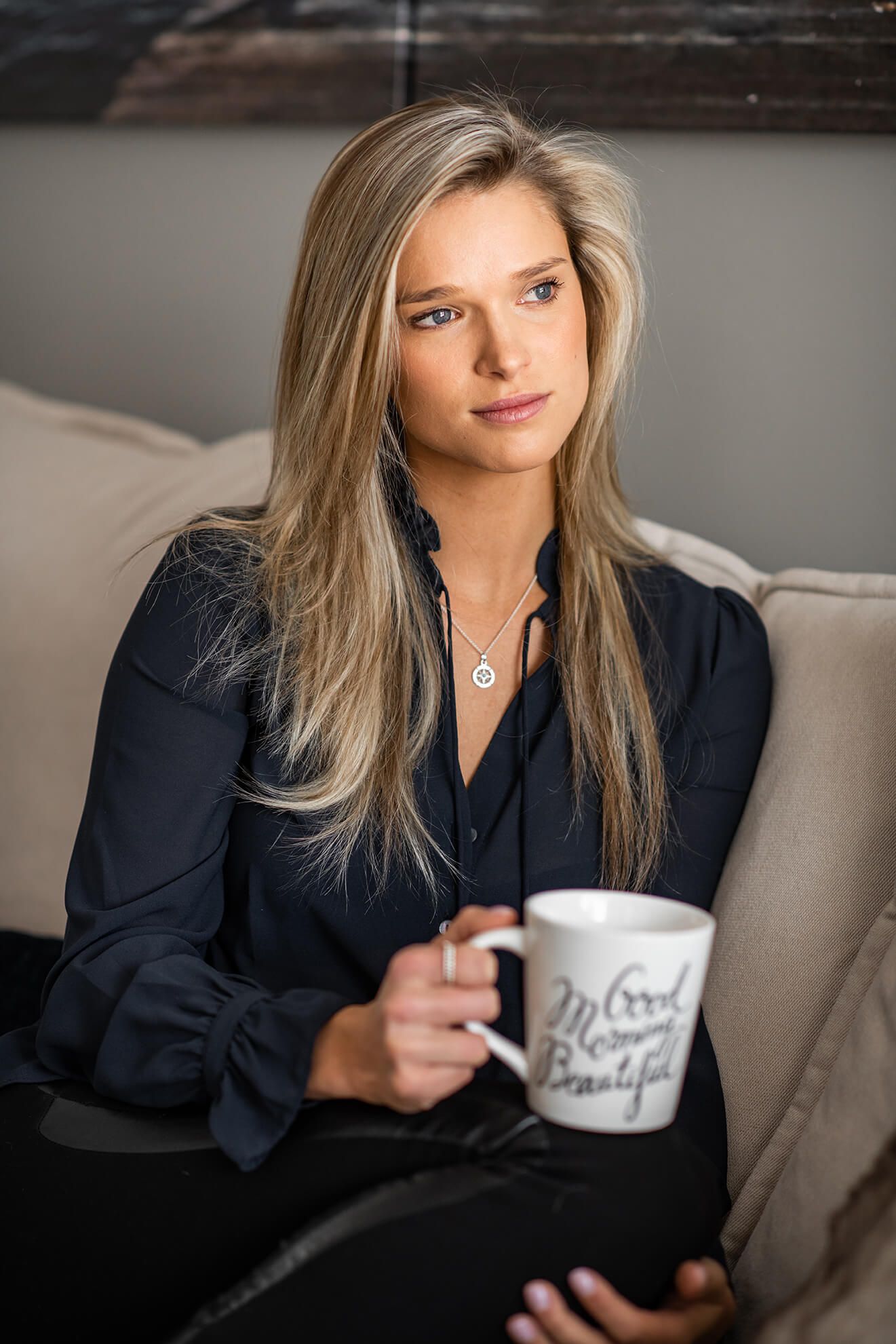 Lifestyle photo of someone in a navy blouse holding a coffee mug while sitting on a gray couch.