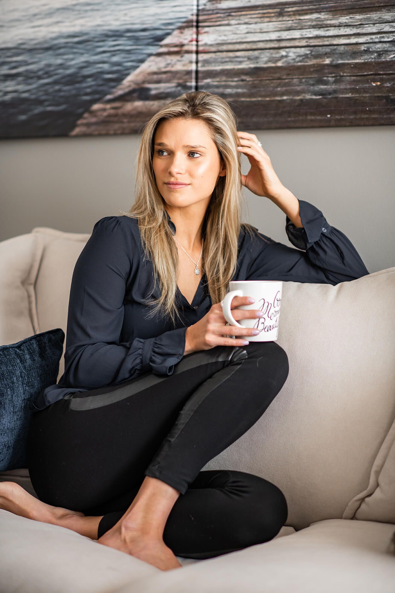 A relaxed lifestyle portrait showing someone in black loungewear holding a coffee mug on a beige couch.