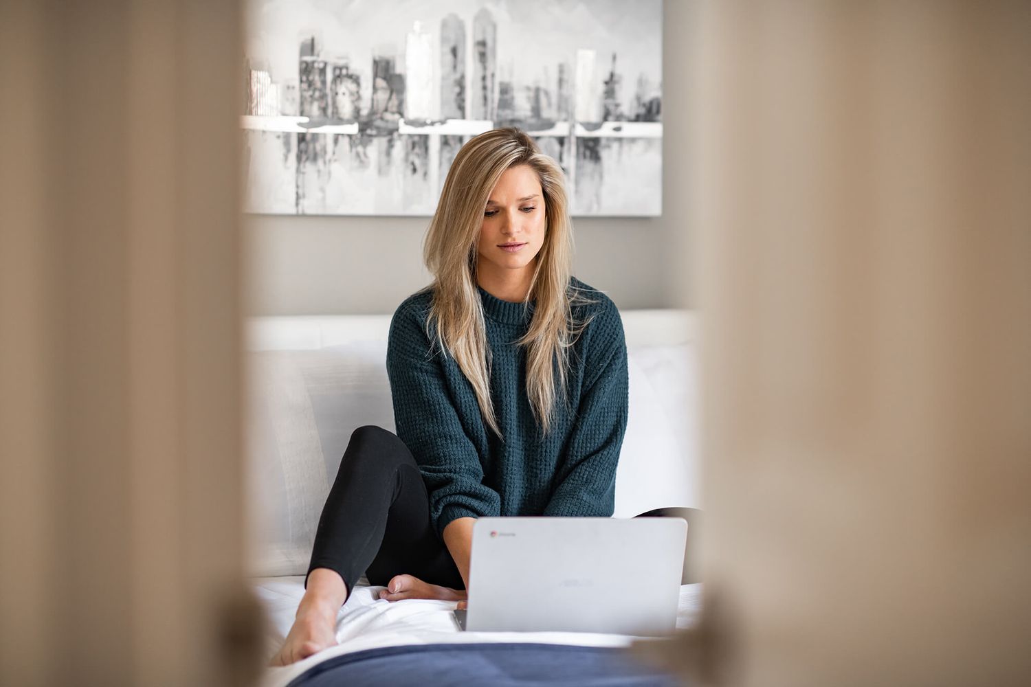 Person in dark sweater working on laptop against grey wall with modern cityscape art.