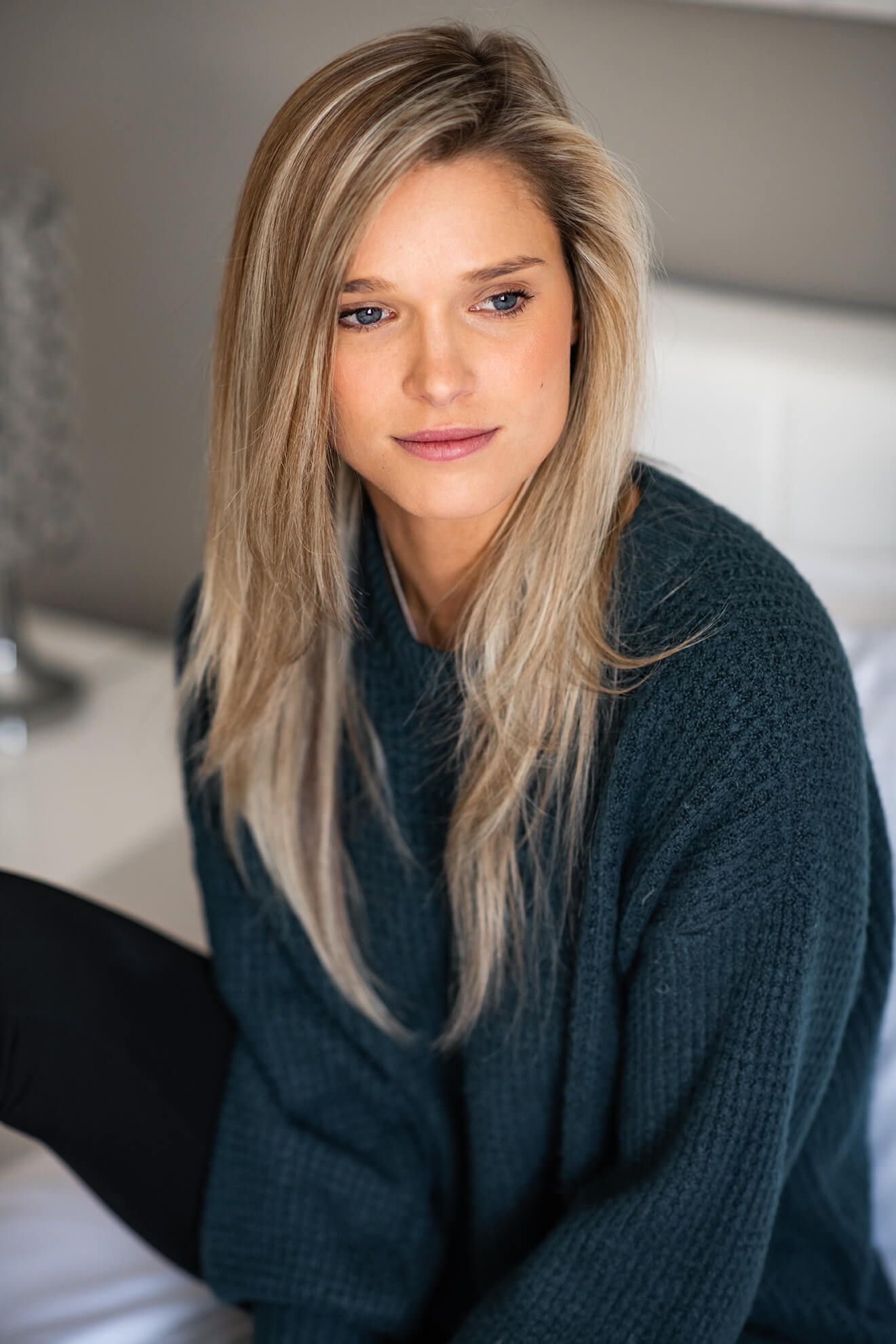 Person in navy knit sweater poses against neutral wall with natural lighting.