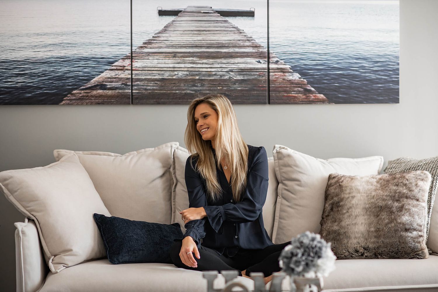 Cozy interior scene with white couch and decorative wall art featuring ocean dock photography.