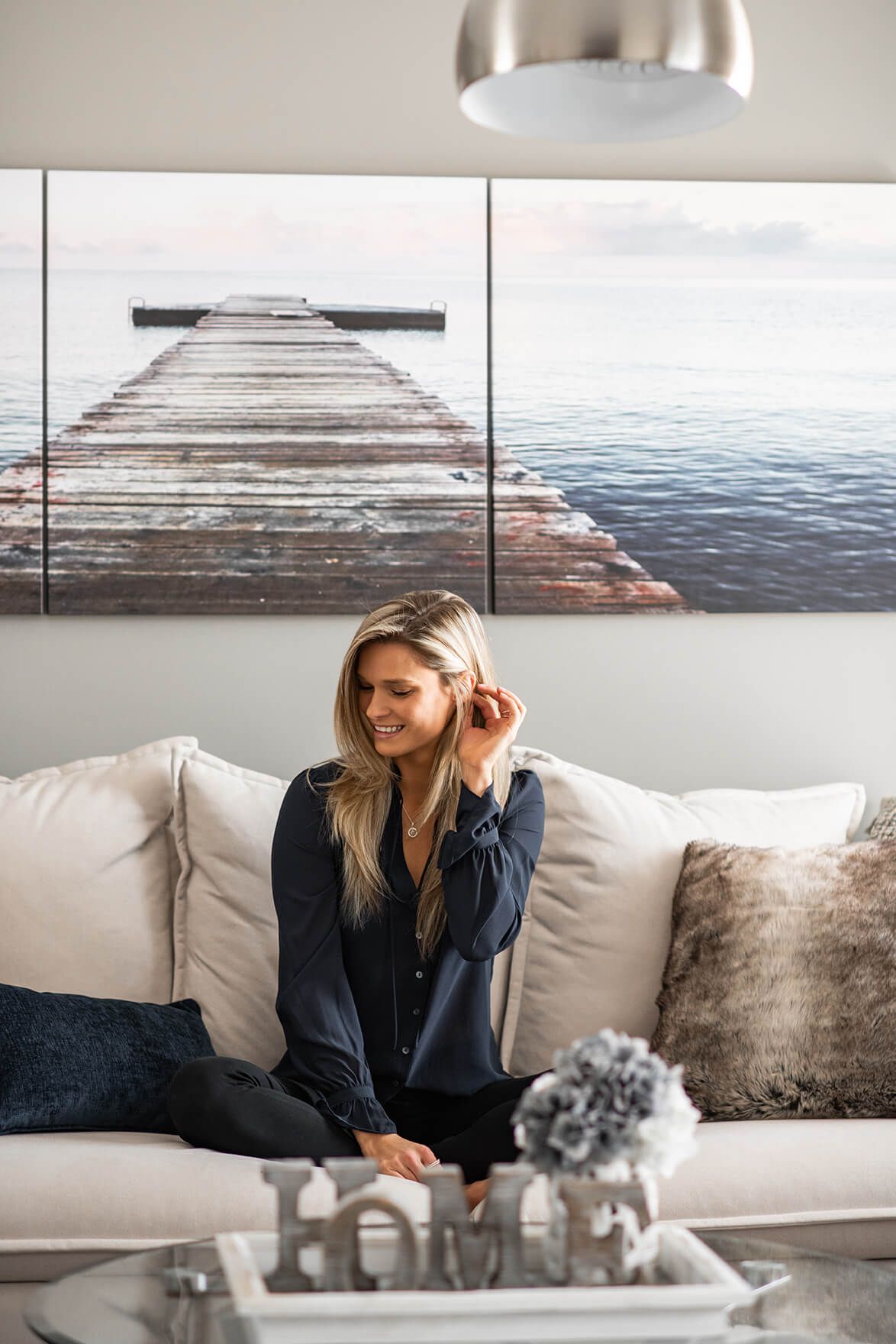 Lifestyle scene showing someone relaxing on white couch with coastal artwork in background.