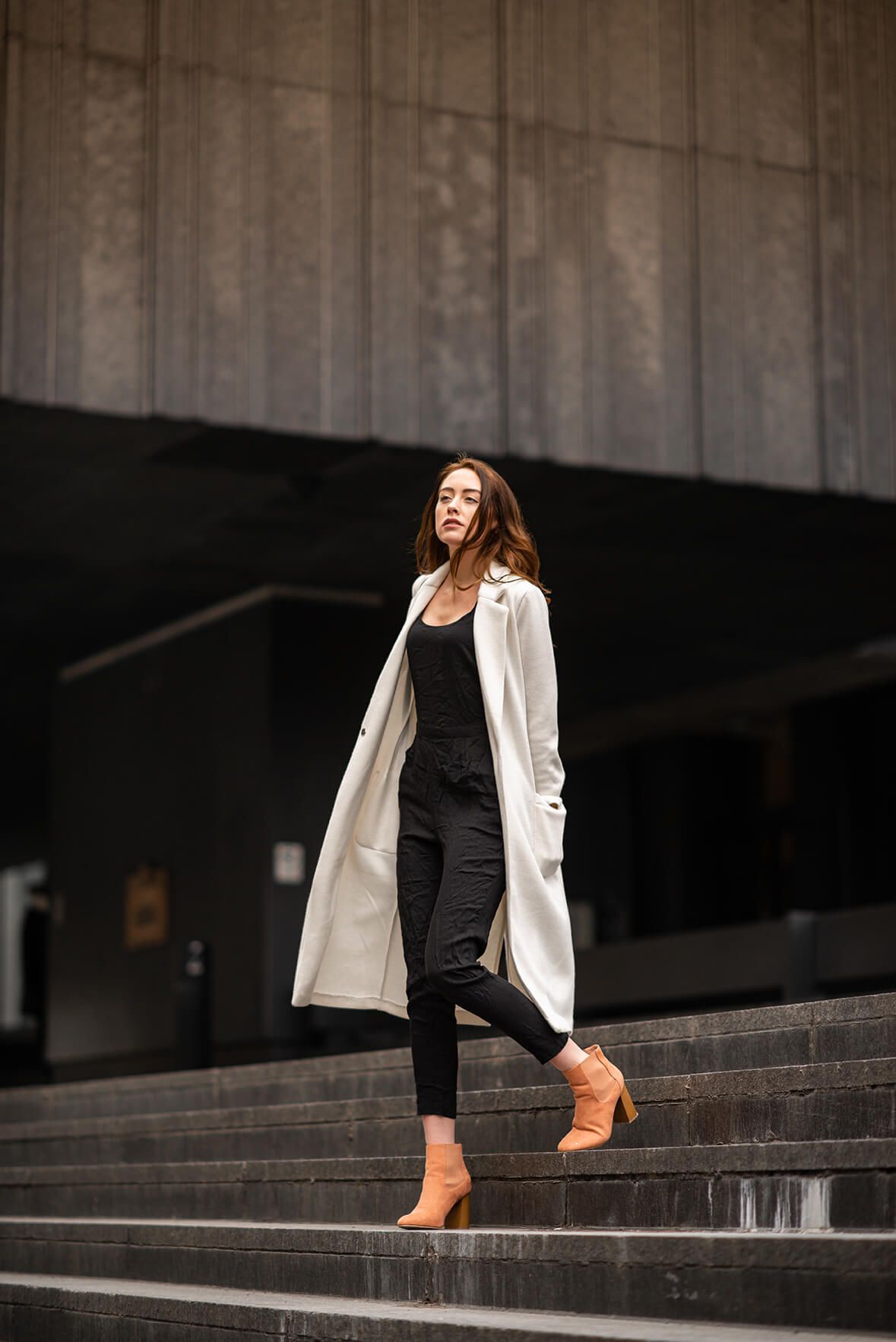 Person in white blazer and black outfit walking down concrete steps in brown boots.