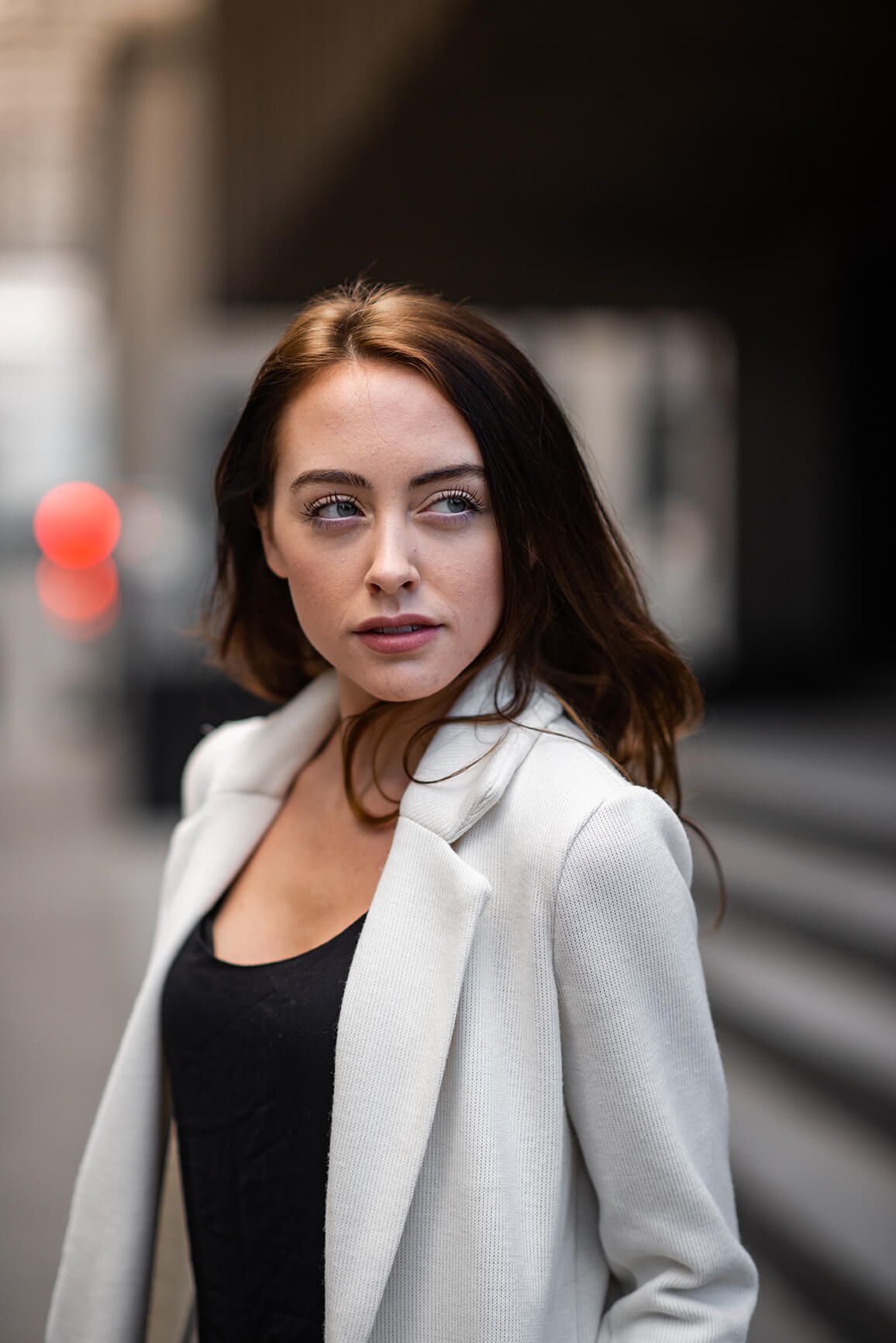 Close-up fashion portrait showcasing a crisp white coat against dark urban background.