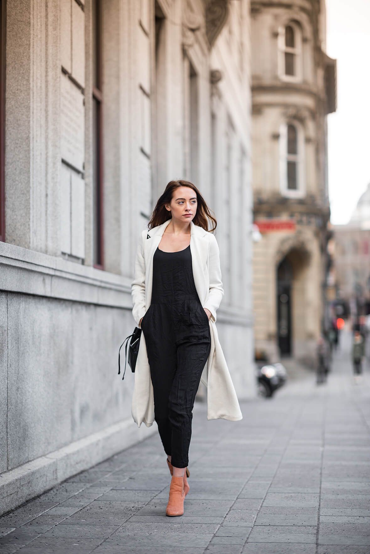 Dynamic fashion shot showing movement in a white blazer and black dress along a city sidewalk.