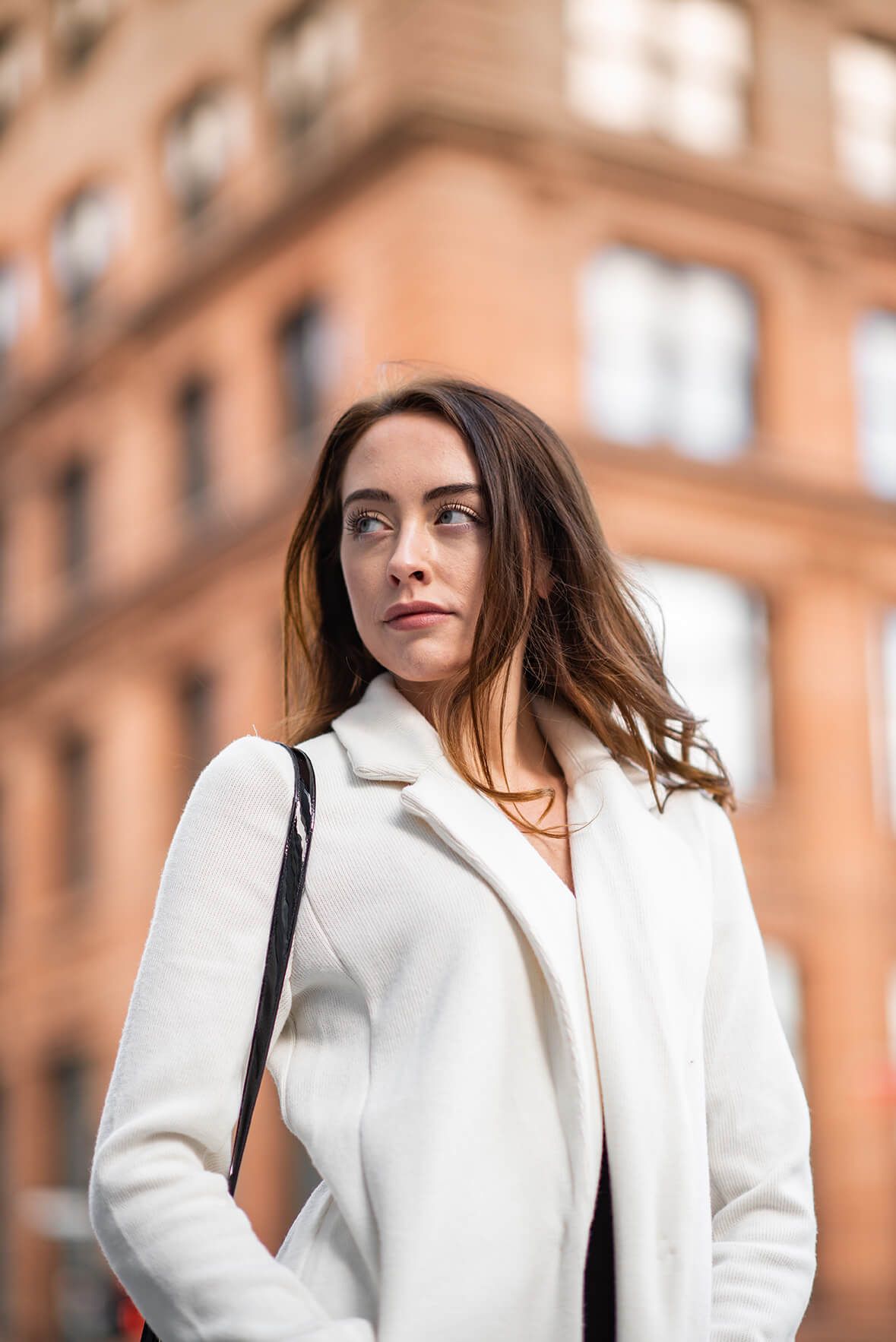 Elegant white coat and dark hair create contrast against warm-toned building architecture.