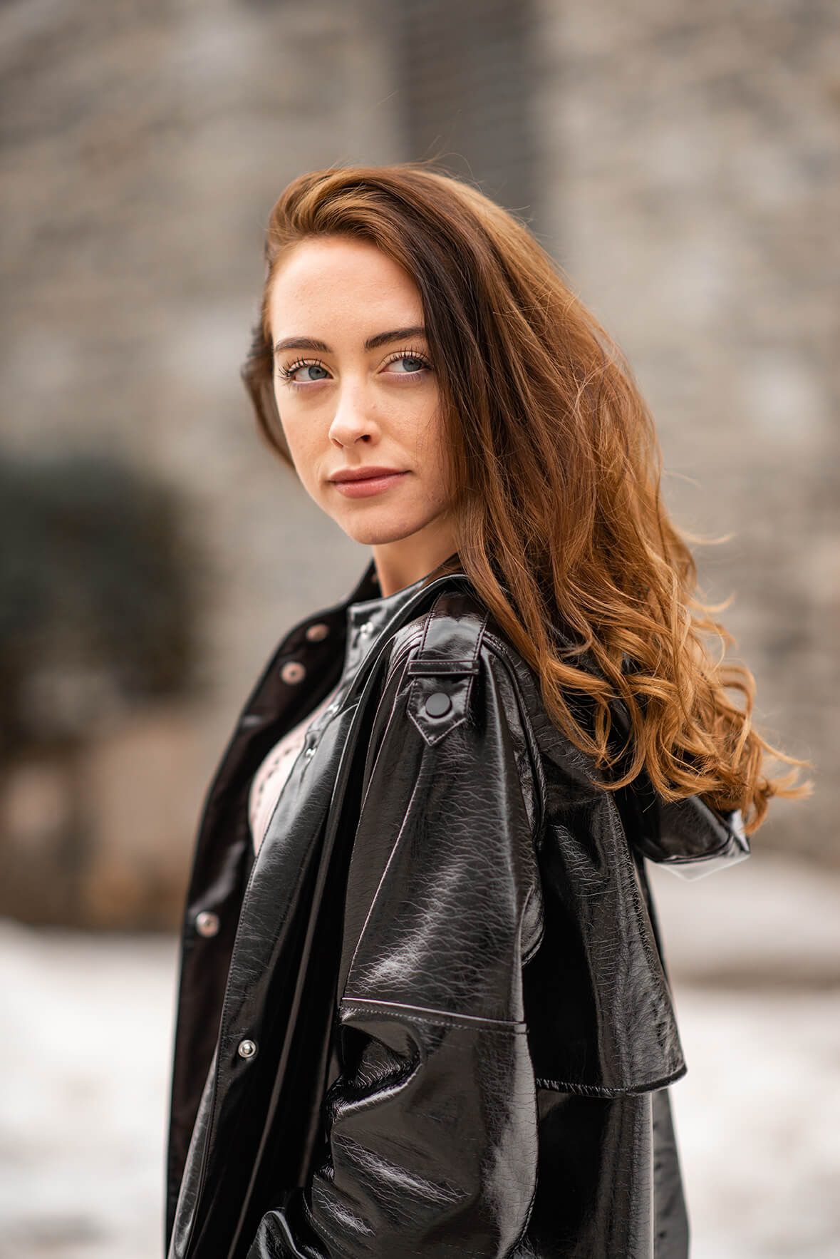 A stylish black leather jacket contrasts with flowing brown hair in an urban winter setting.