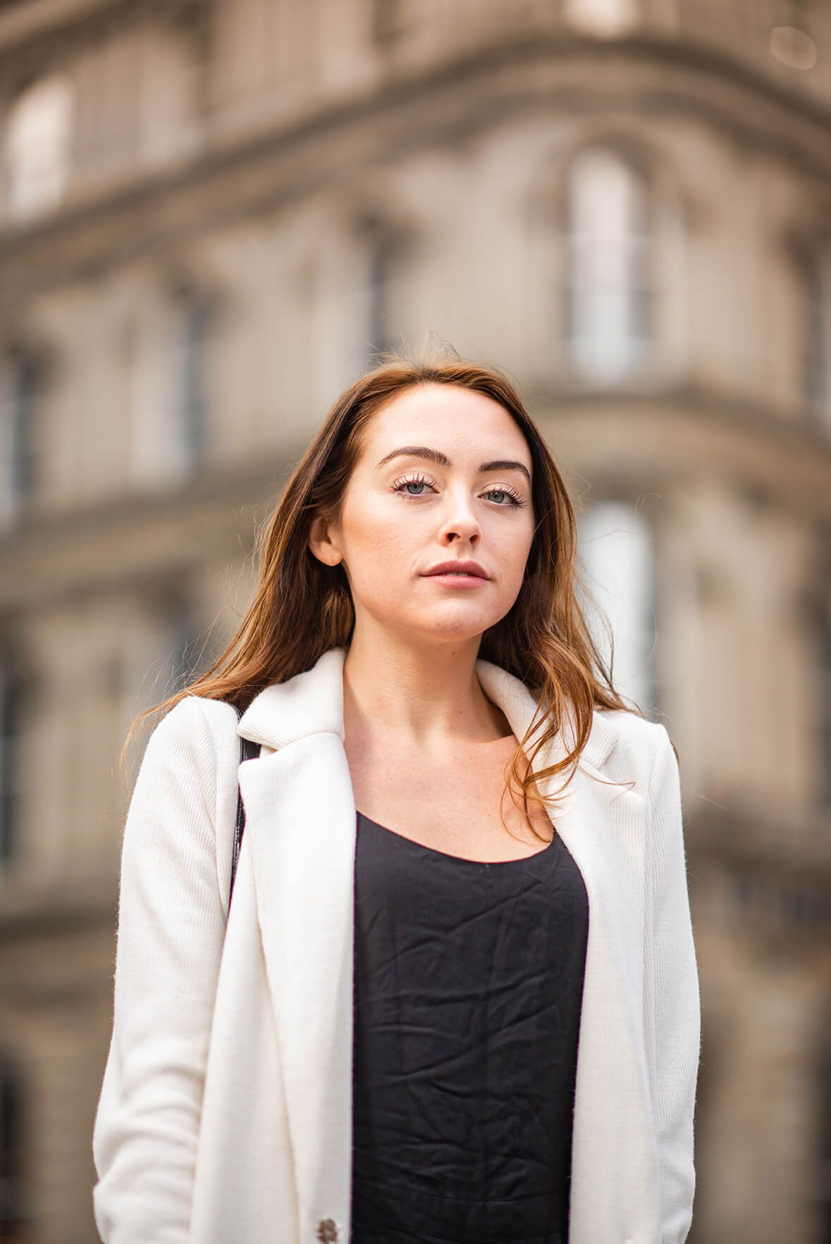 Professional portrait featuring a white blazer and black top against an architectural backdrop.