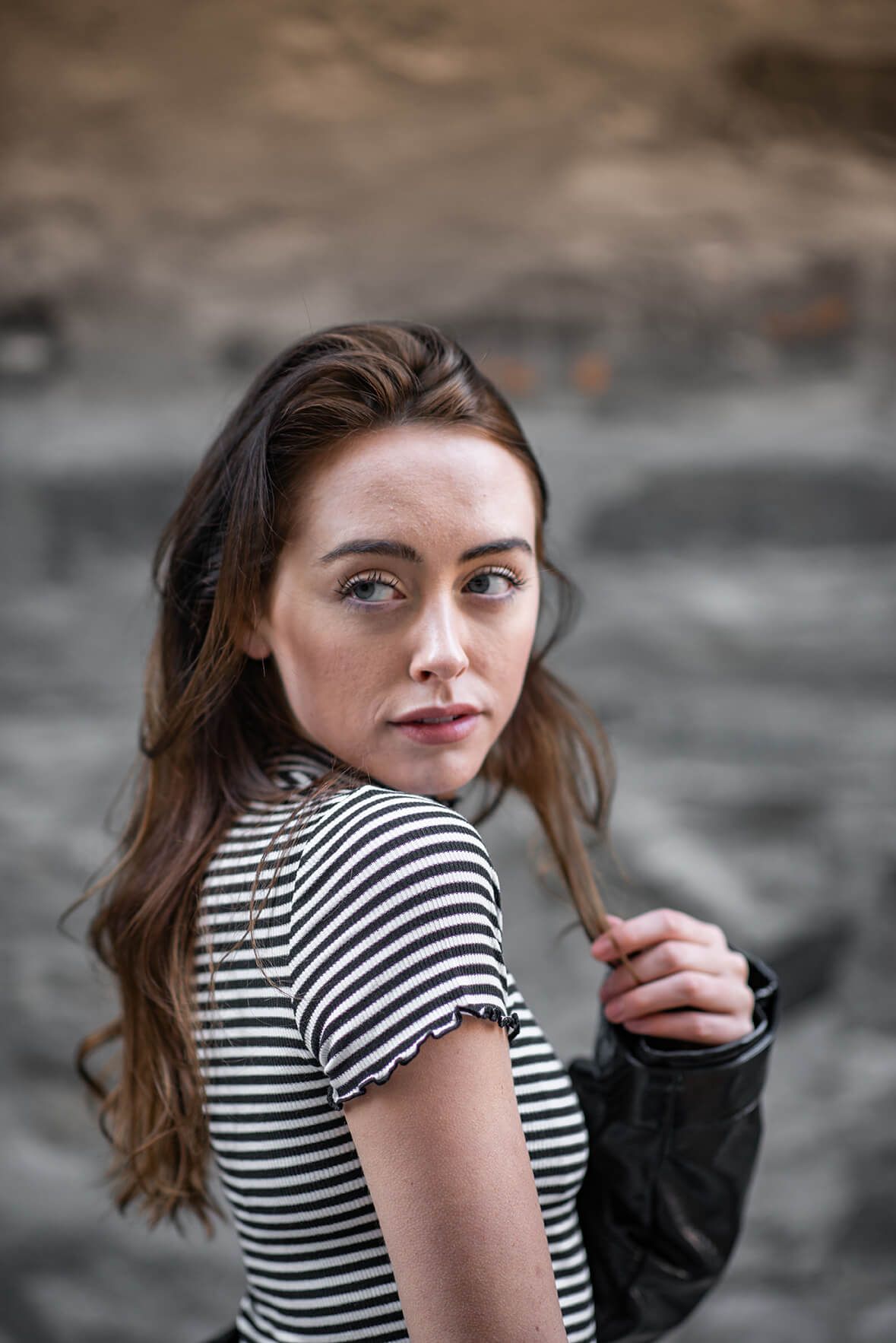 Casual portrait in striped shirt with leather jacket against textured wall.