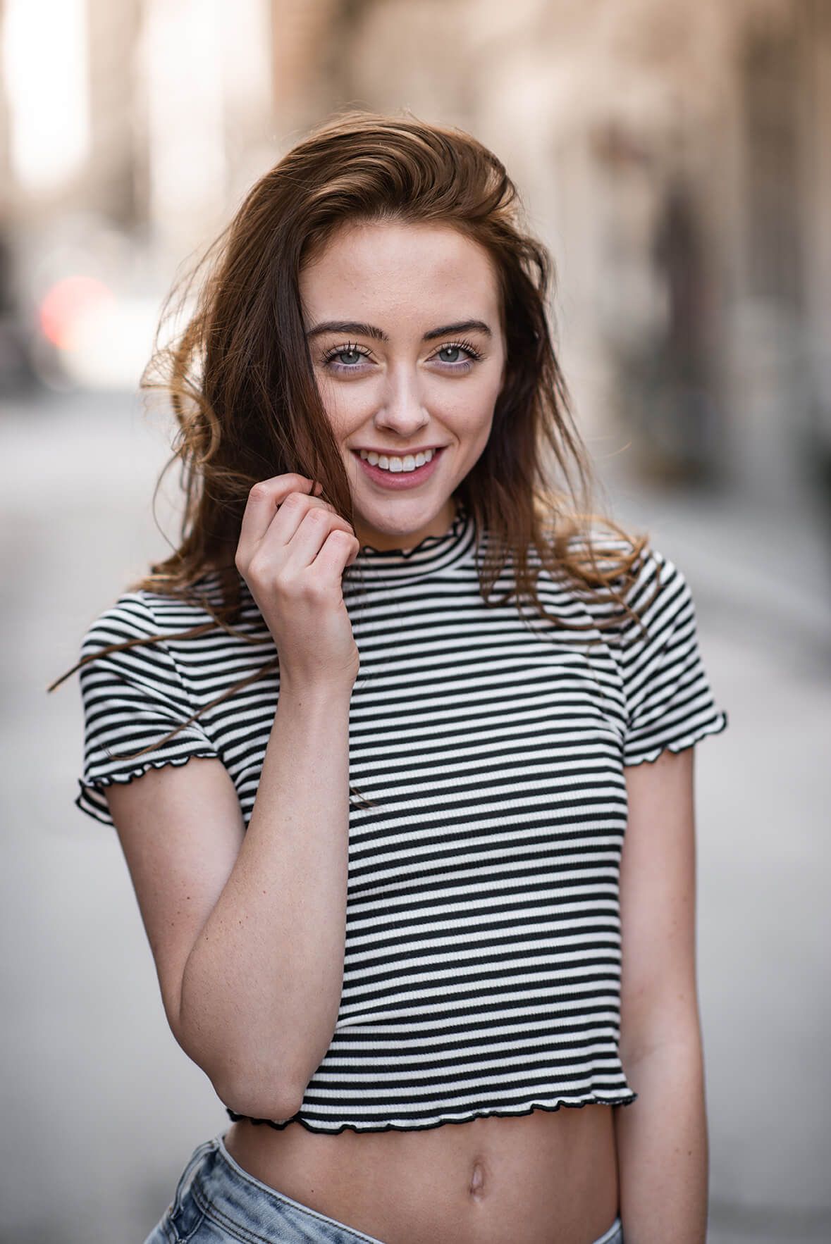 Young woman in striped crop top smiling on urban street.