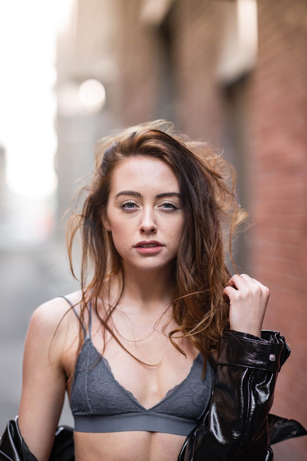 Dramatic portrait in grey top with windswept hair against blurred background.