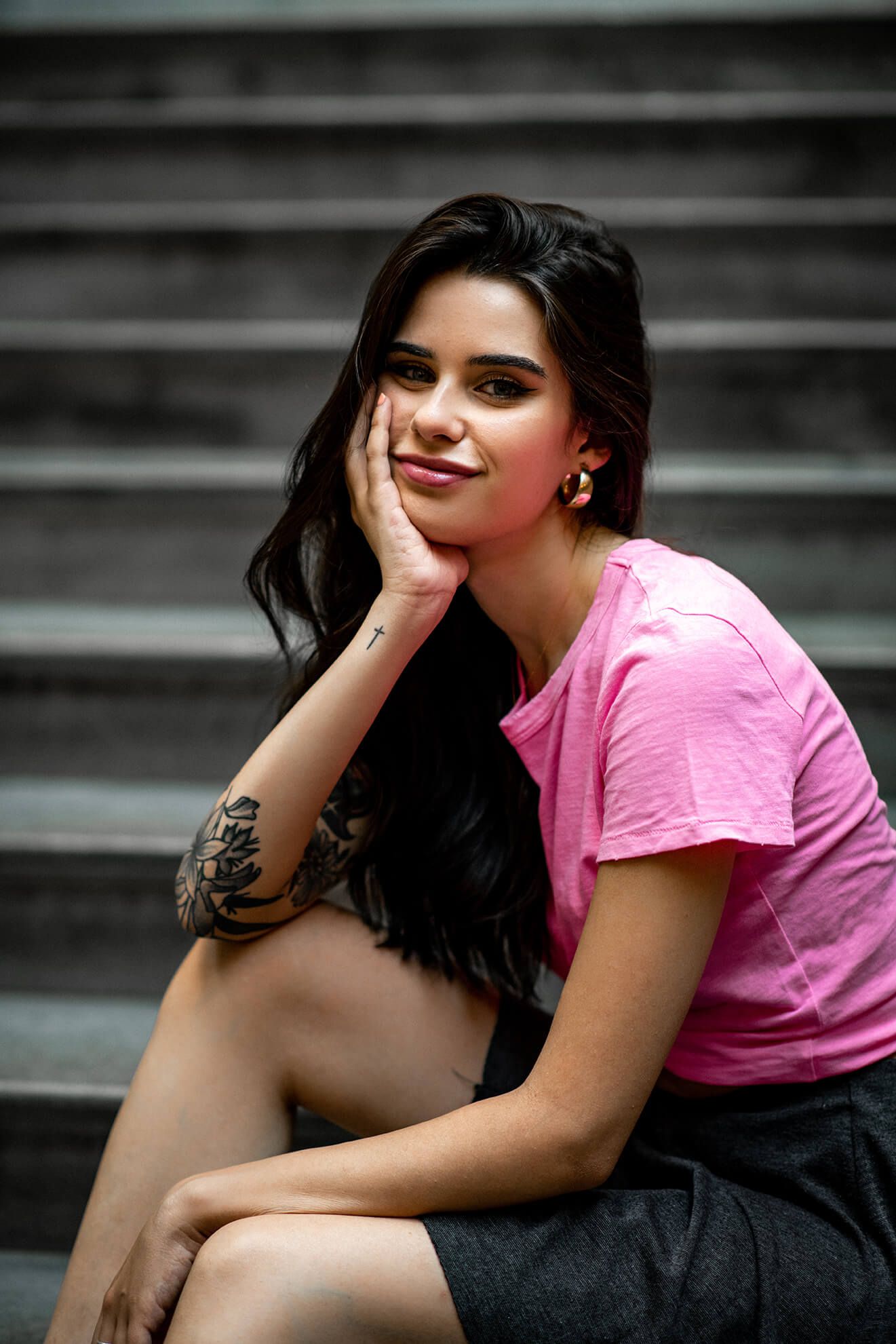 Artistic portrait on concrete steps with pink shirt and dark styling.