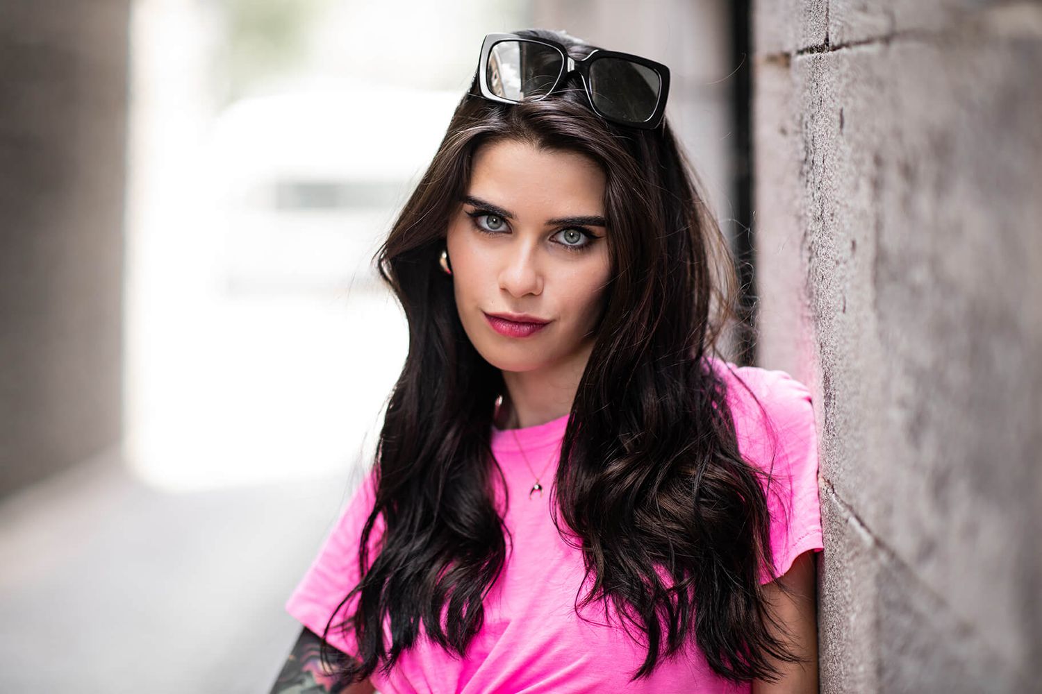 A fashion portrait in pink and black against a concrete wall with dramatic lighting and shadows.