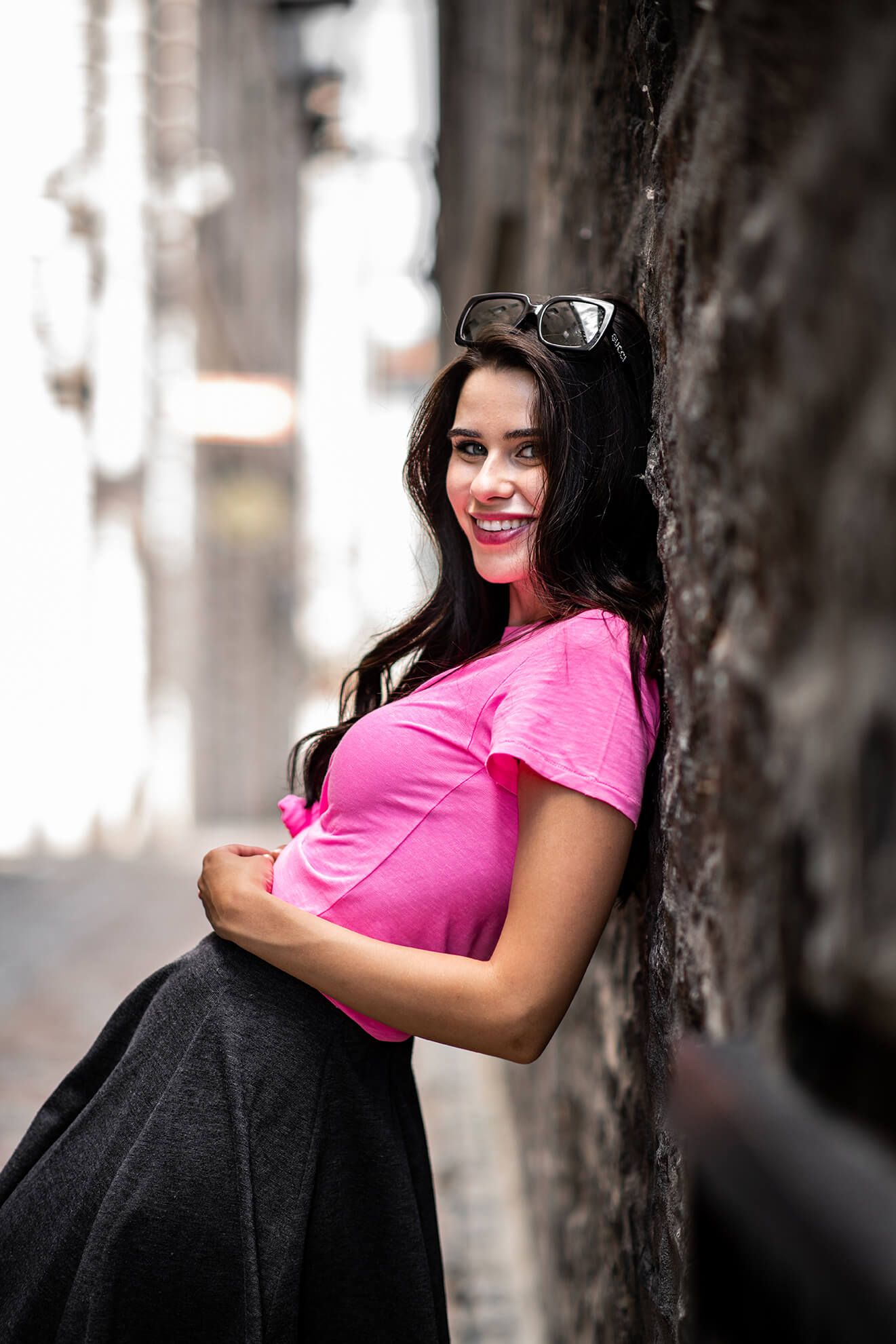 Casual street style look with pink top and black skirt against stone wall.