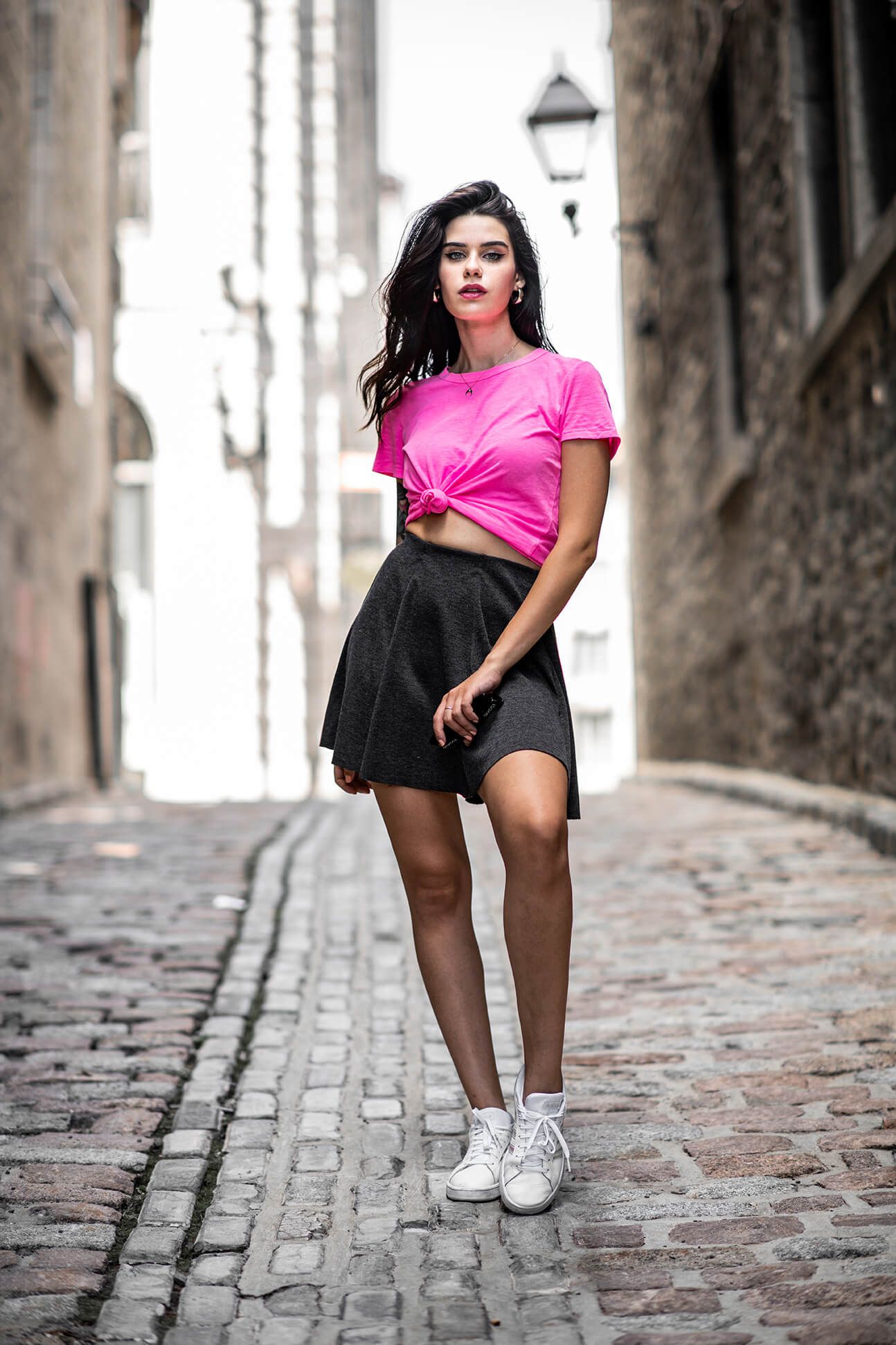 Urban fashion photography on cobblestone street with white sneakers and pink top.