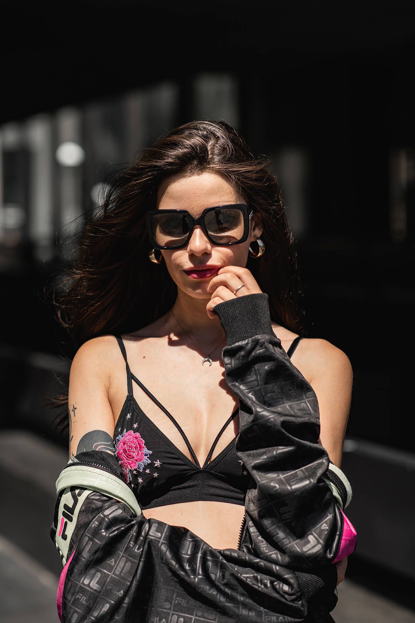 Stylish street fashion with sunglasses and embroidered black bralette against dark background.