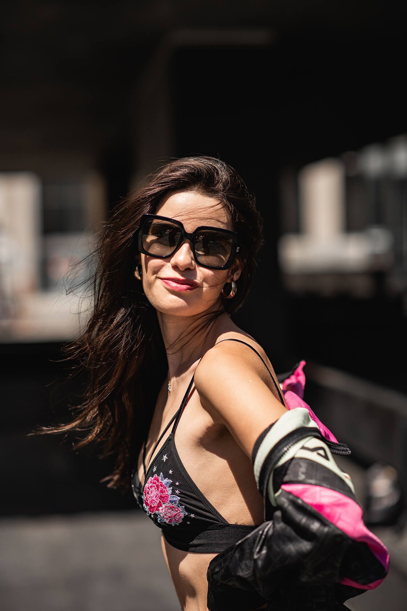 Summer street style with black bralette and vintage jacket in sunlit urban setting.