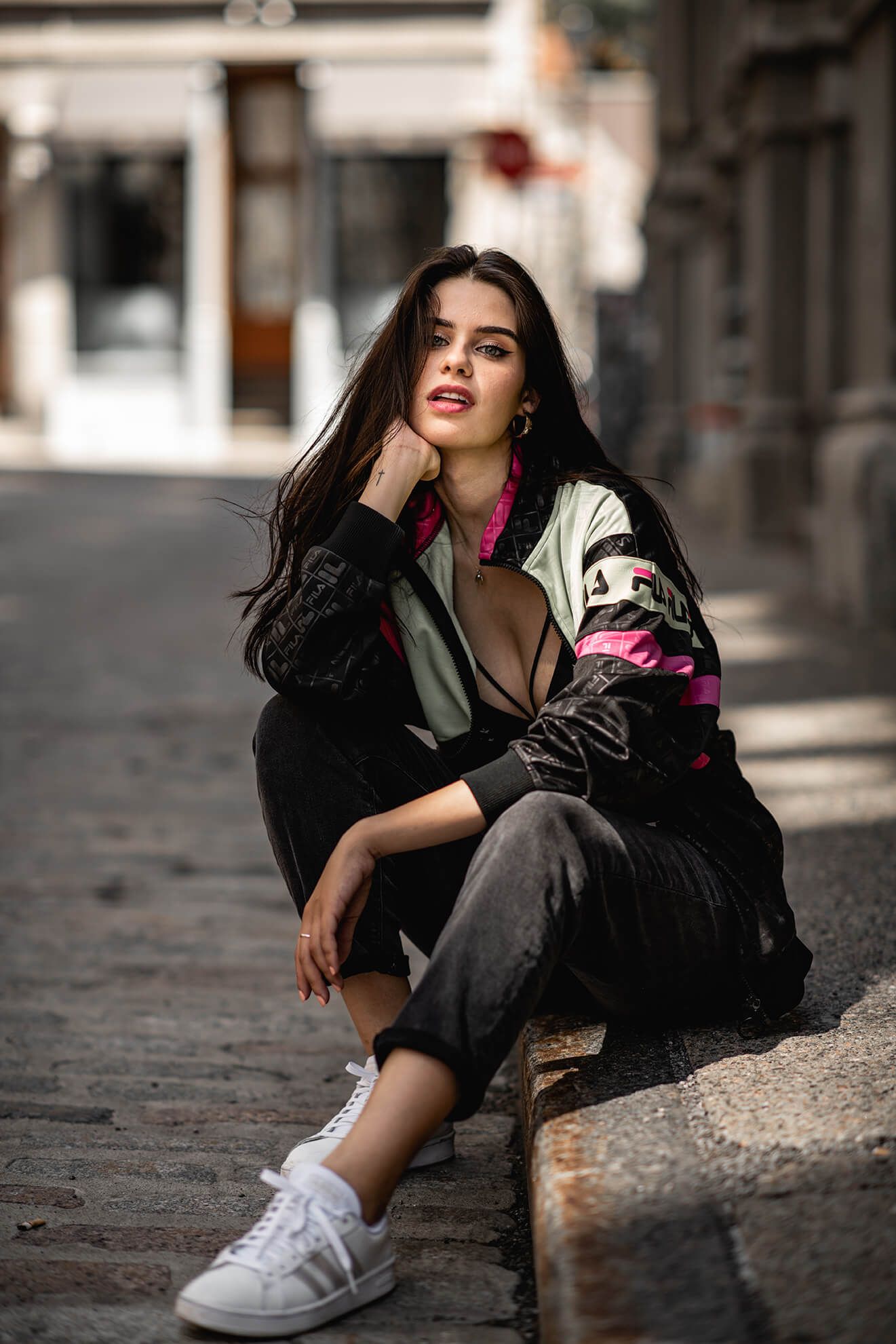 Urban fashion portrait featuring a sporty FILA jacket and white sneakers on a cobblestone street.