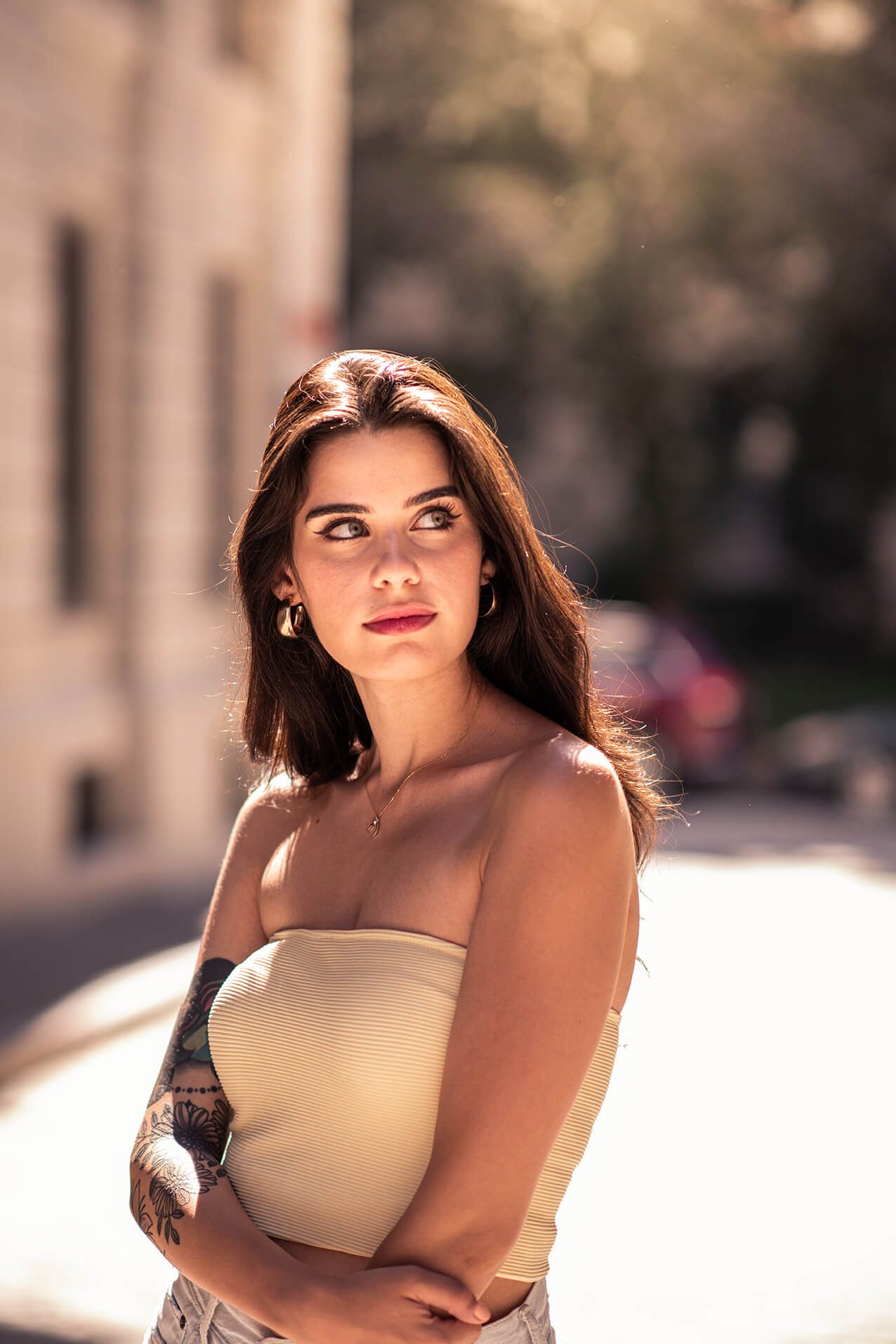 A person poses outdoors in natural lighting wearing a neutral-colored top.