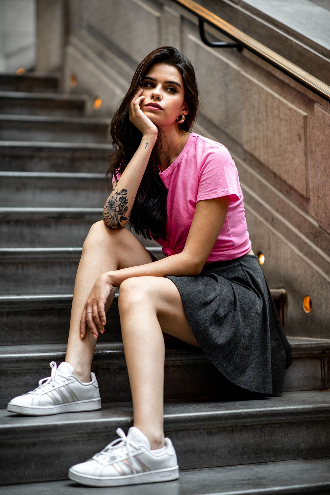 A person rests on urban steps wearing casual attire and white athletic shoes.