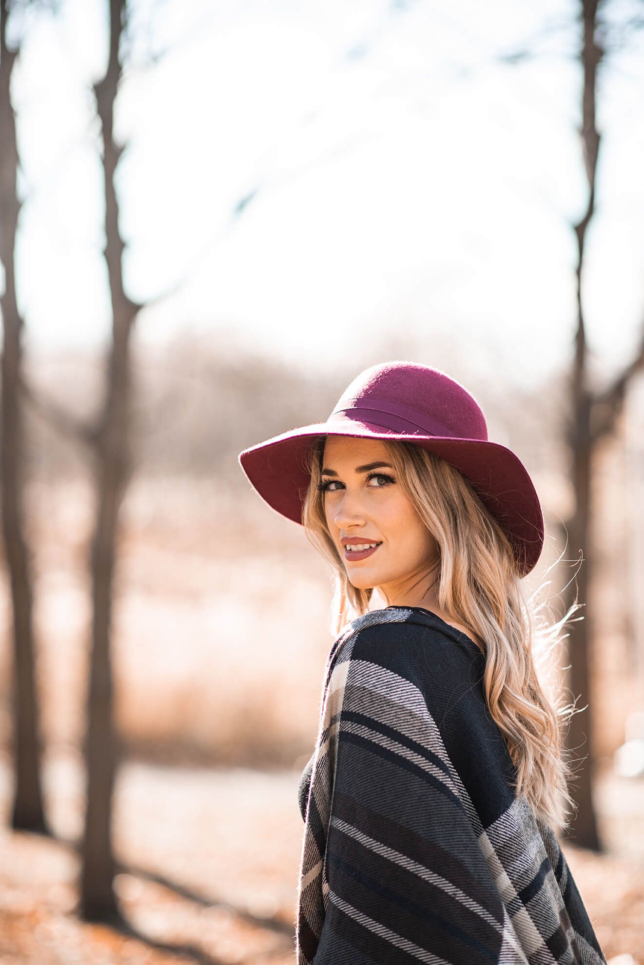 Stylish outdoor portrait with burgundy hat and wrapped plaid shawl in muted tones.