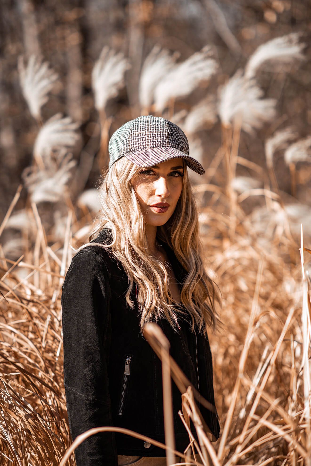 Outdoor portrait with warm tones featuring checkered cap and black sweater.