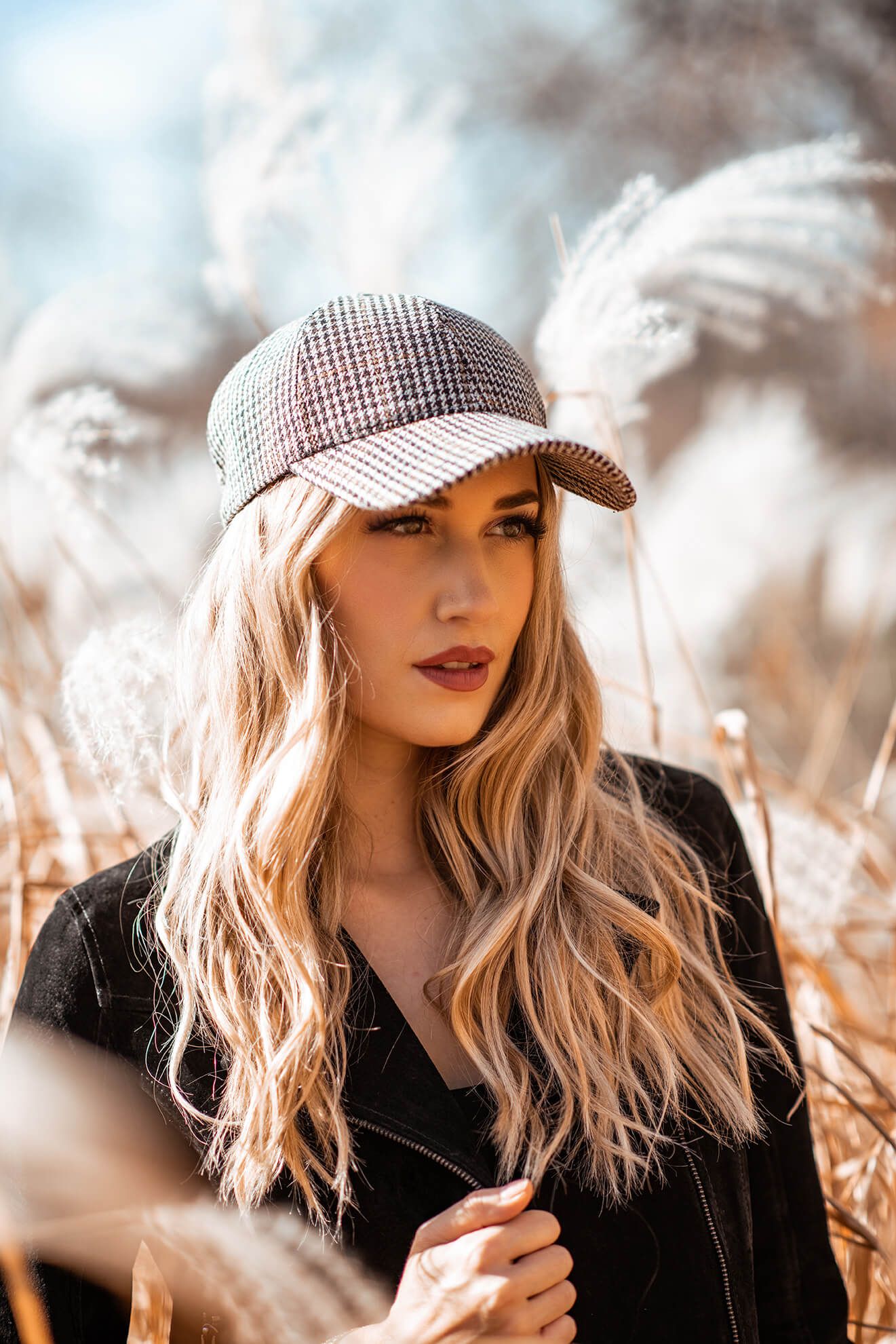 Fashion portrait with checkered cap and black top against natural dried grass backdrop.