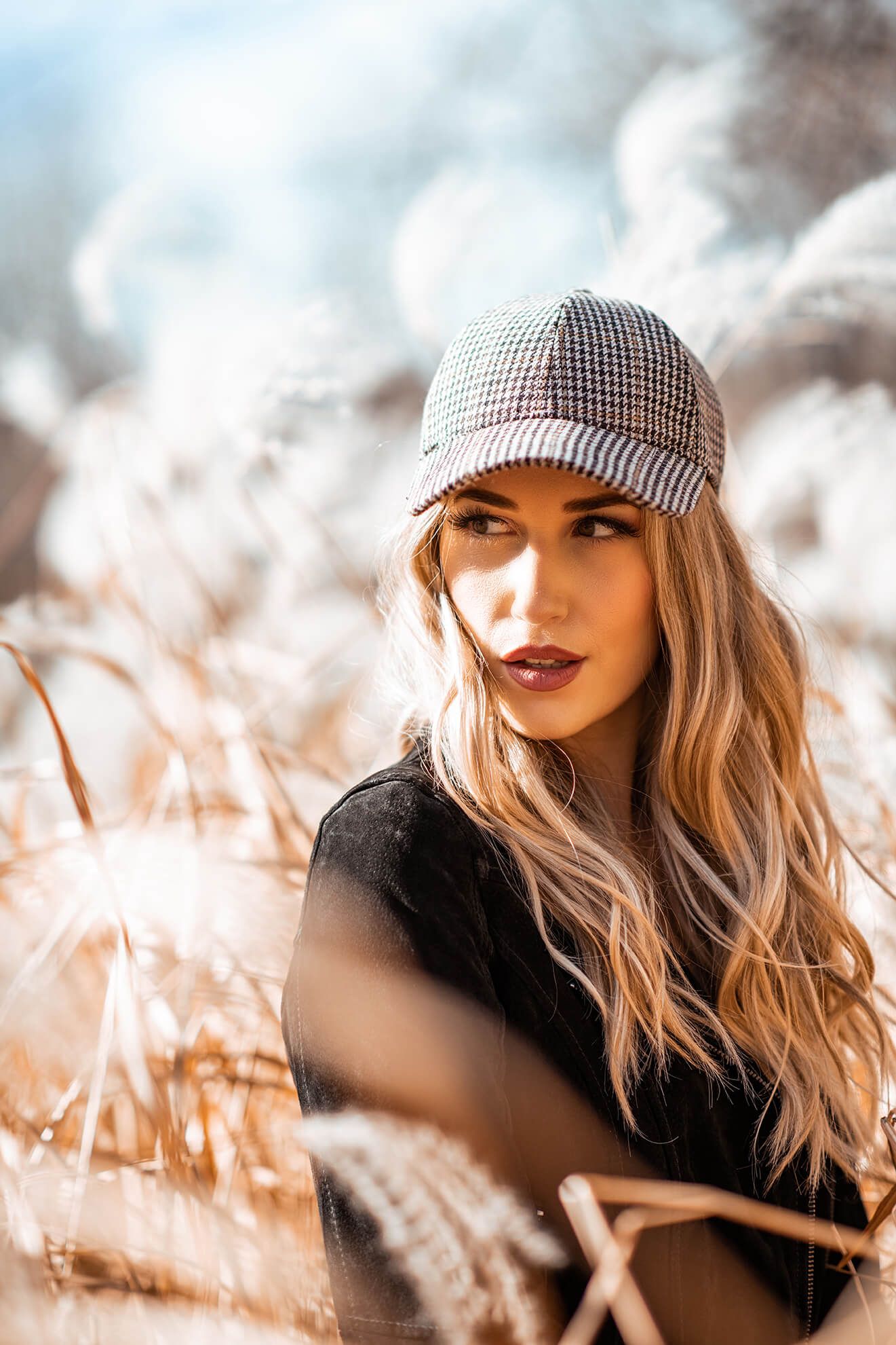 Stylish autumn portrait wearing checkered cap among dried grass with soft lighting.
