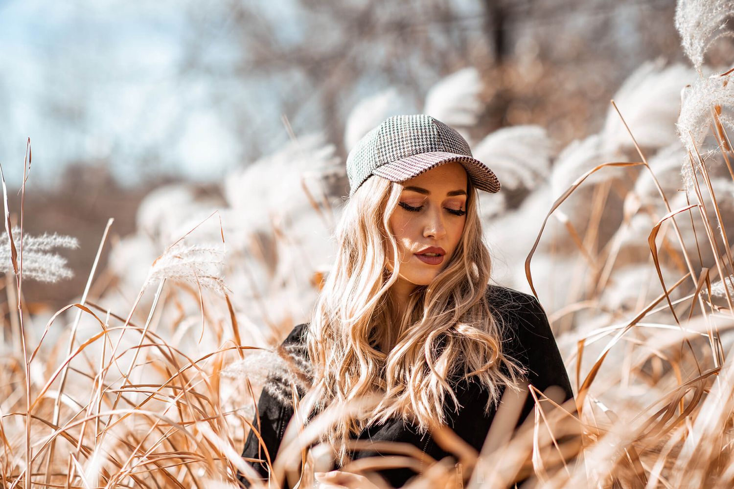 Outdoor fashion portrait featuring woman in baseball cap among dried grass.