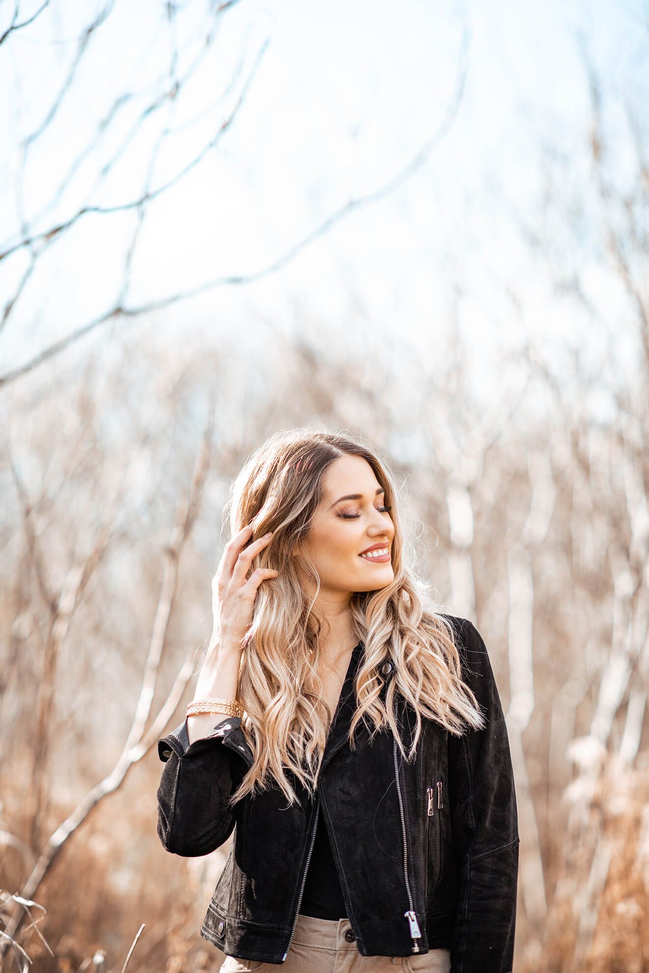 Natural light portrait of woman in black jacket enjoying a carefree moment outdoors.