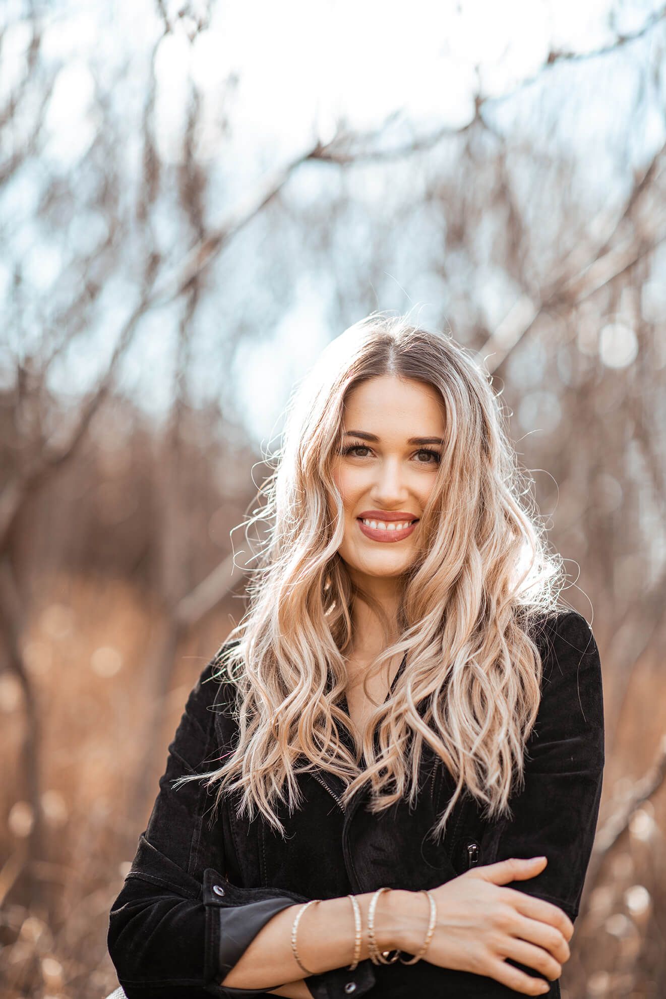 Candid lifestyle portrait showing woman in black top with tousled blonde hair smiling outdoors.