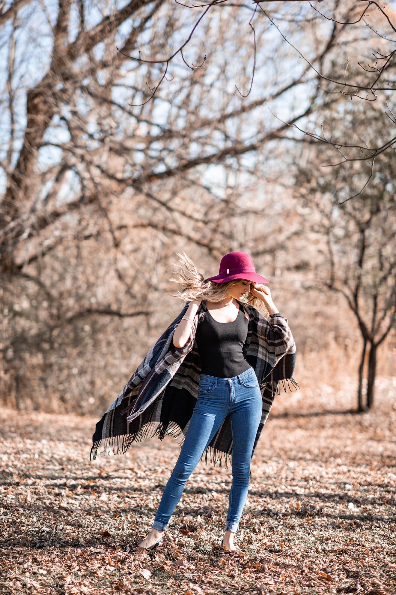 Dynamic dancing poses in autumn leaves wearing a burgundy hat and black jacket.