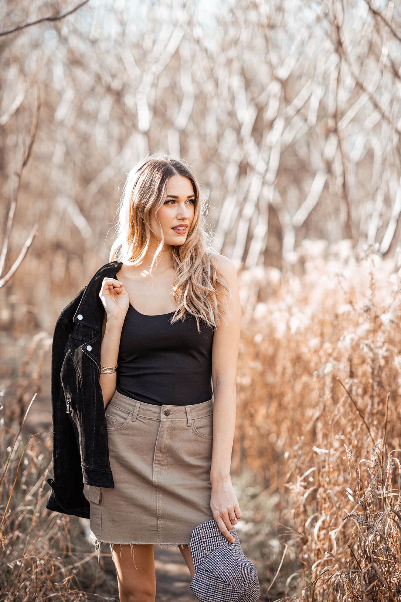 Fashion portrait in autumn setting with black top and tan skirt among dried grass.