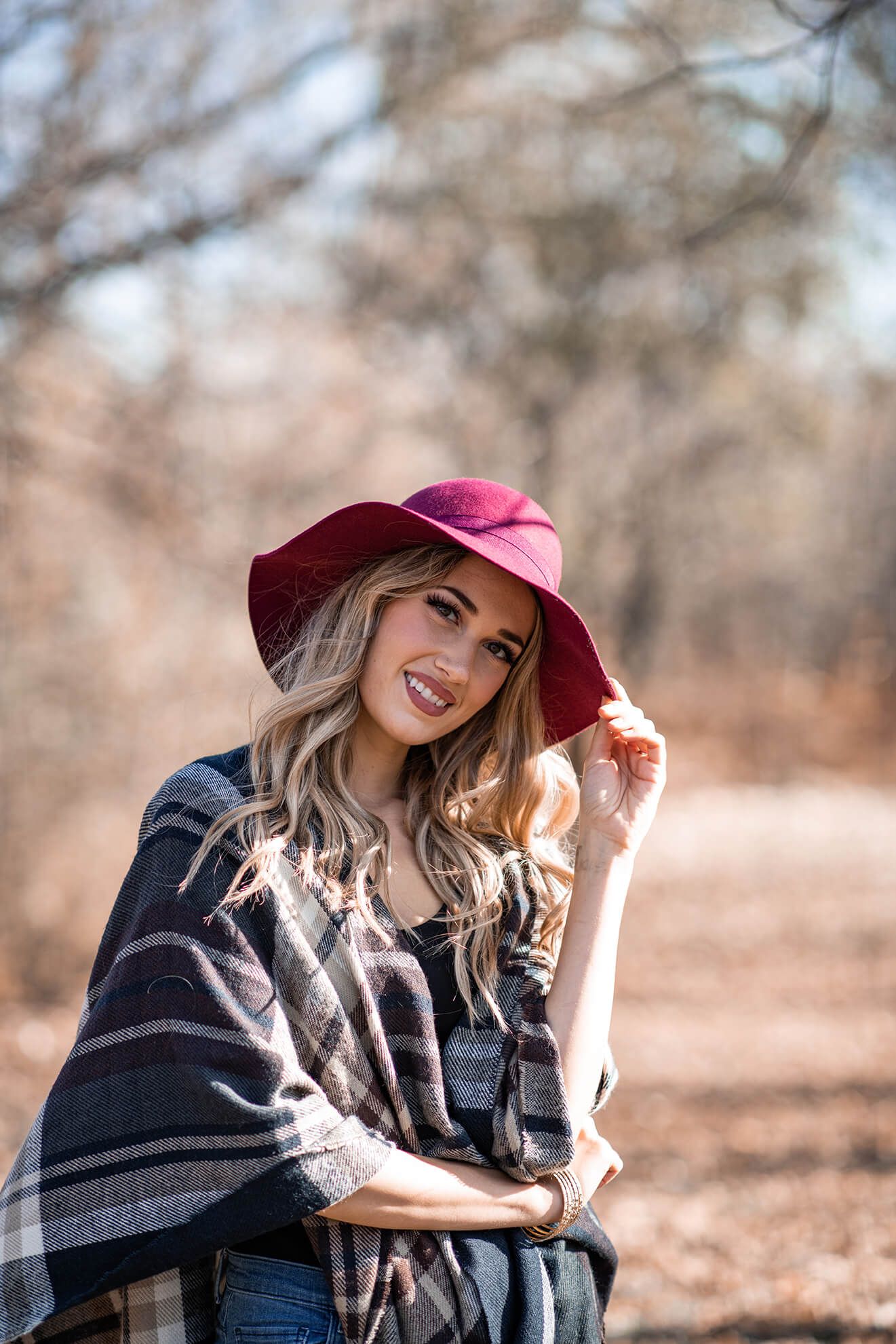 Fashion portrait with plaid wrap and burgundy hat in autumn scenery.