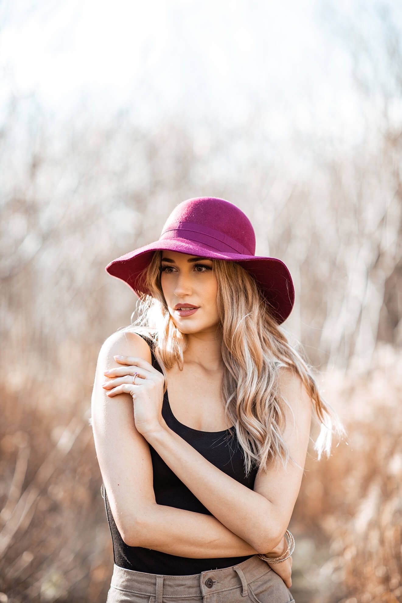 Elegant pose in burgundy hat and black top against soft natural lighting.