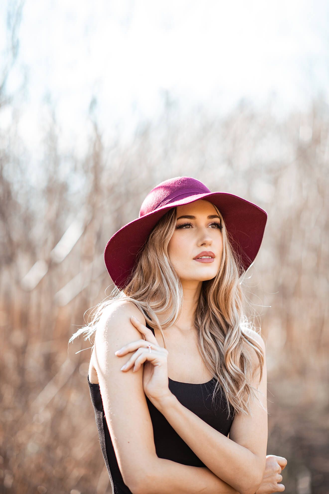 Outdoor portrait featuring a burgundy wide-brim hat against a natural autumn backdrop.