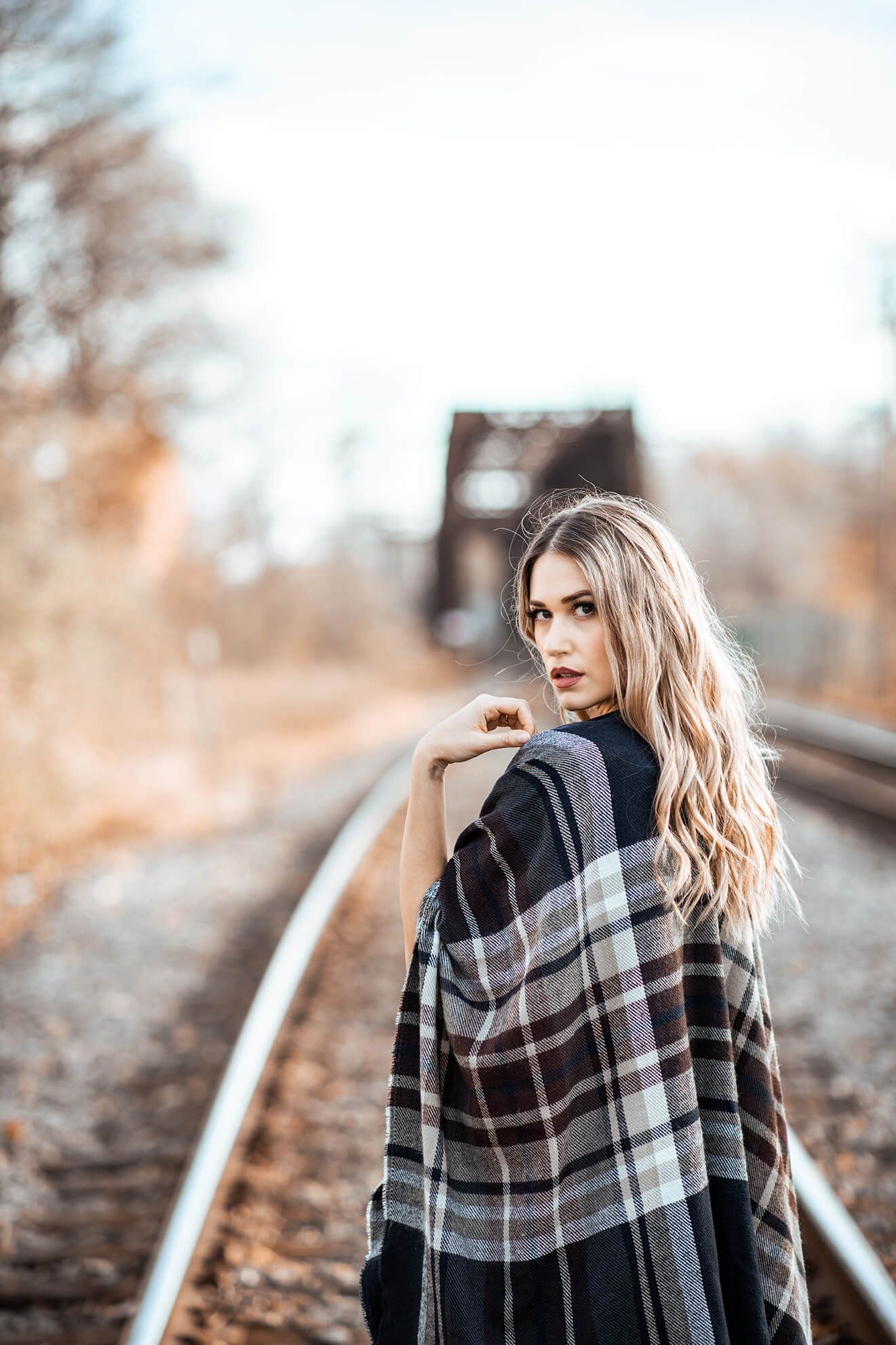 Fashion portrait of someone wearing a plaid scarf on railroad tracks in autumn.