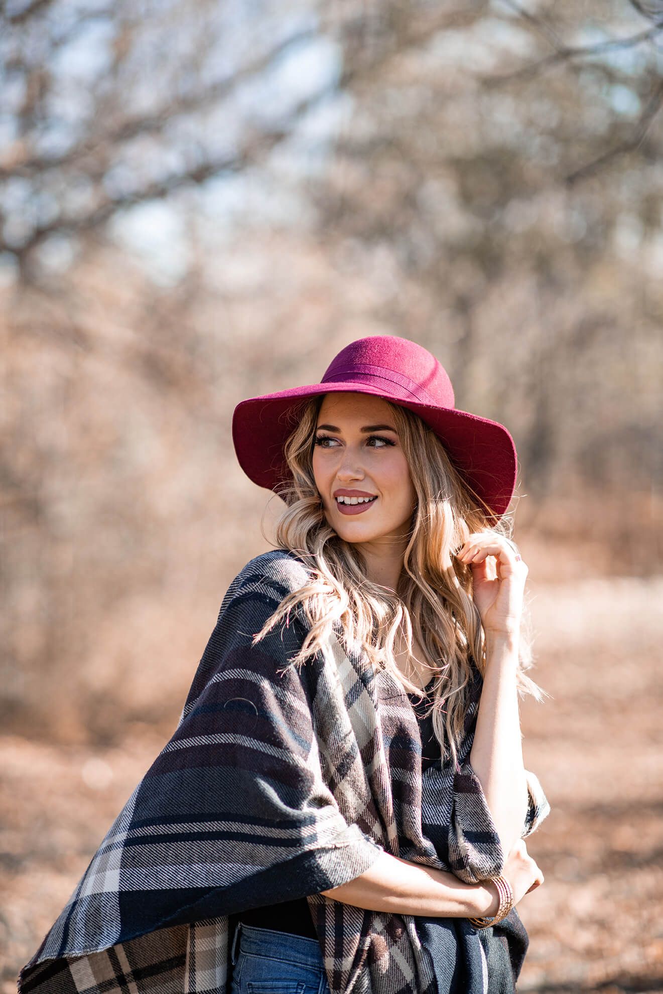 Autumn fashion shoot with burgundy hat and plaid wrap in natural setting.