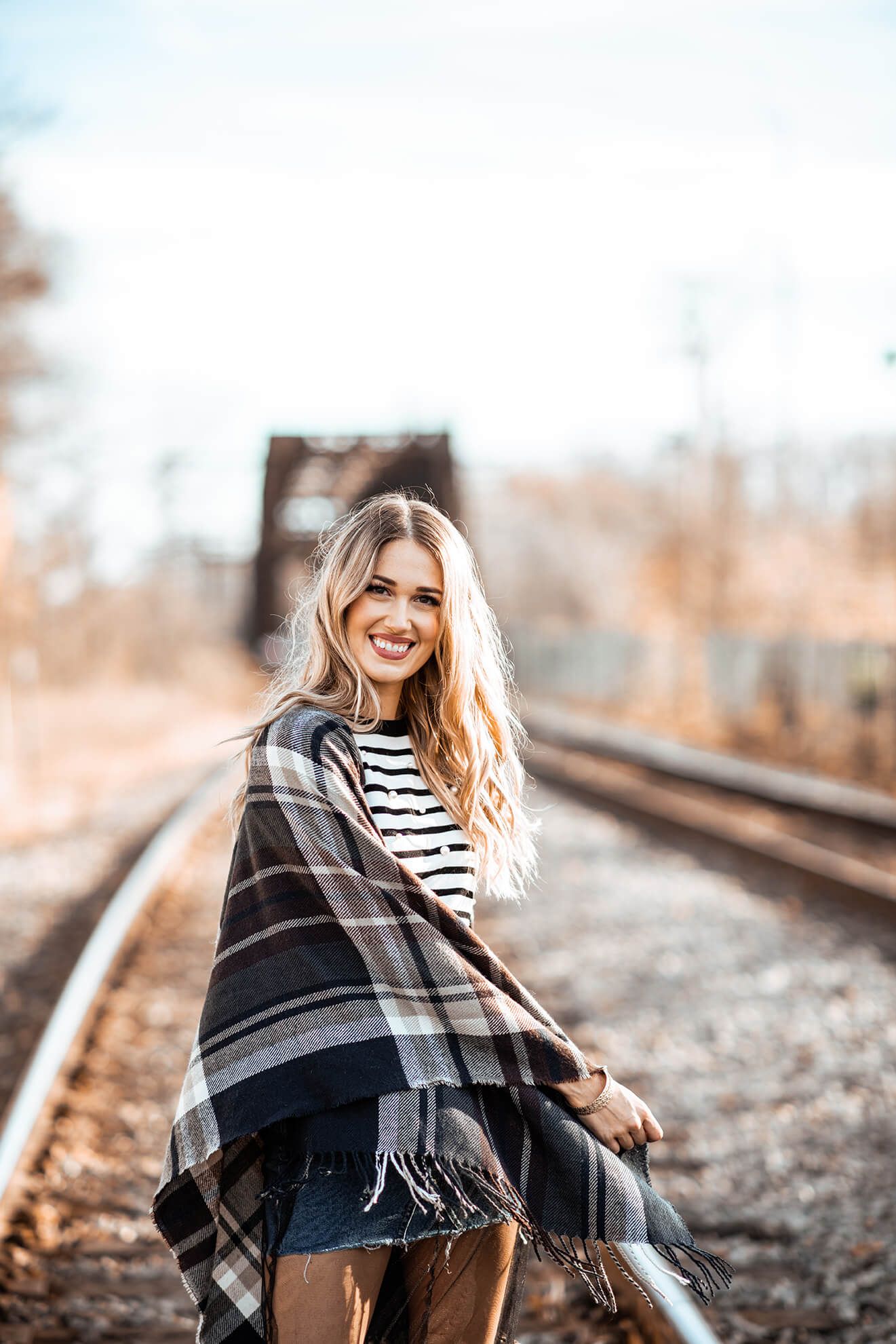 Joyful outdoor fashion portrait on train tracks with plaid wrap.