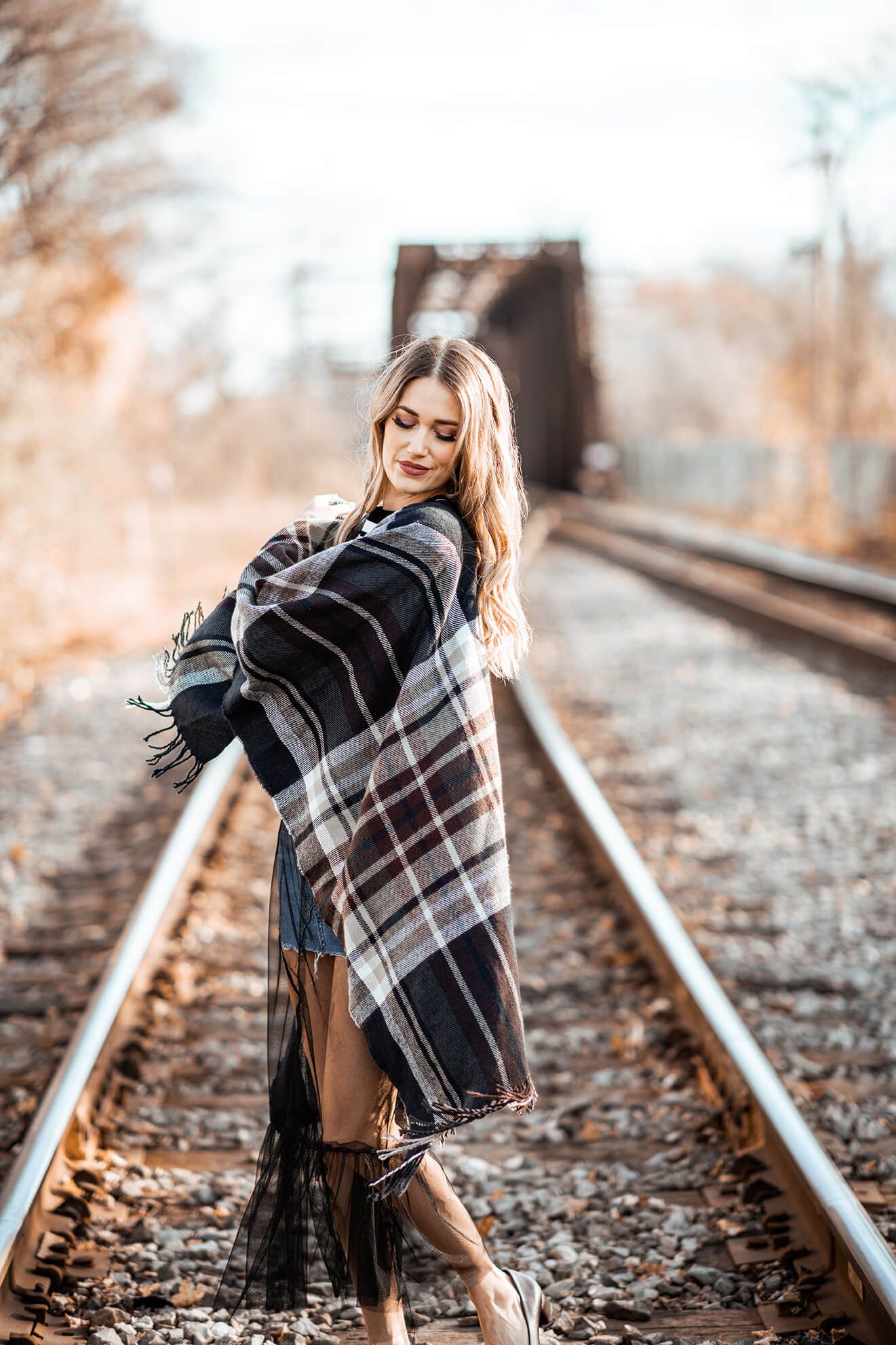 Artistic fashion photo on railway tracks with plaid wrap and denim.