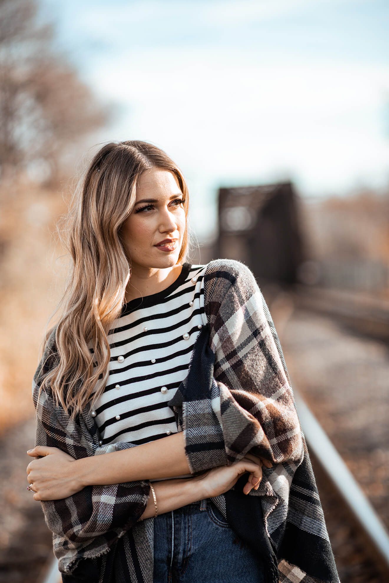 Casual style with striped shirt and plaid wrap on railroad tracks.
