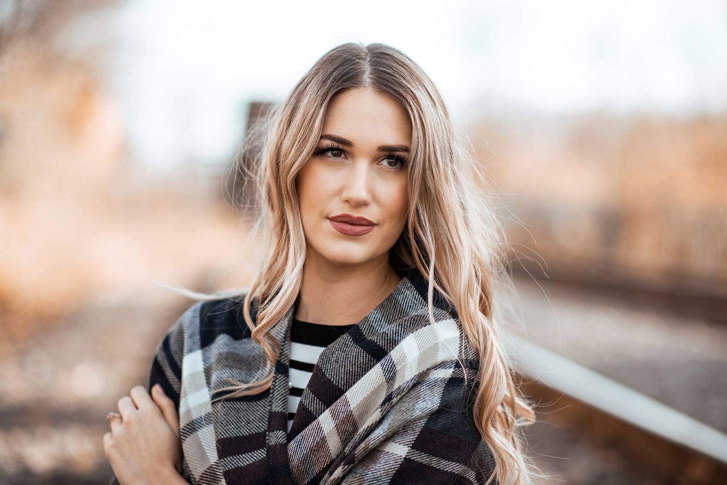 Fashion portrait with plaid scarf and striped top against autumn backdrop.