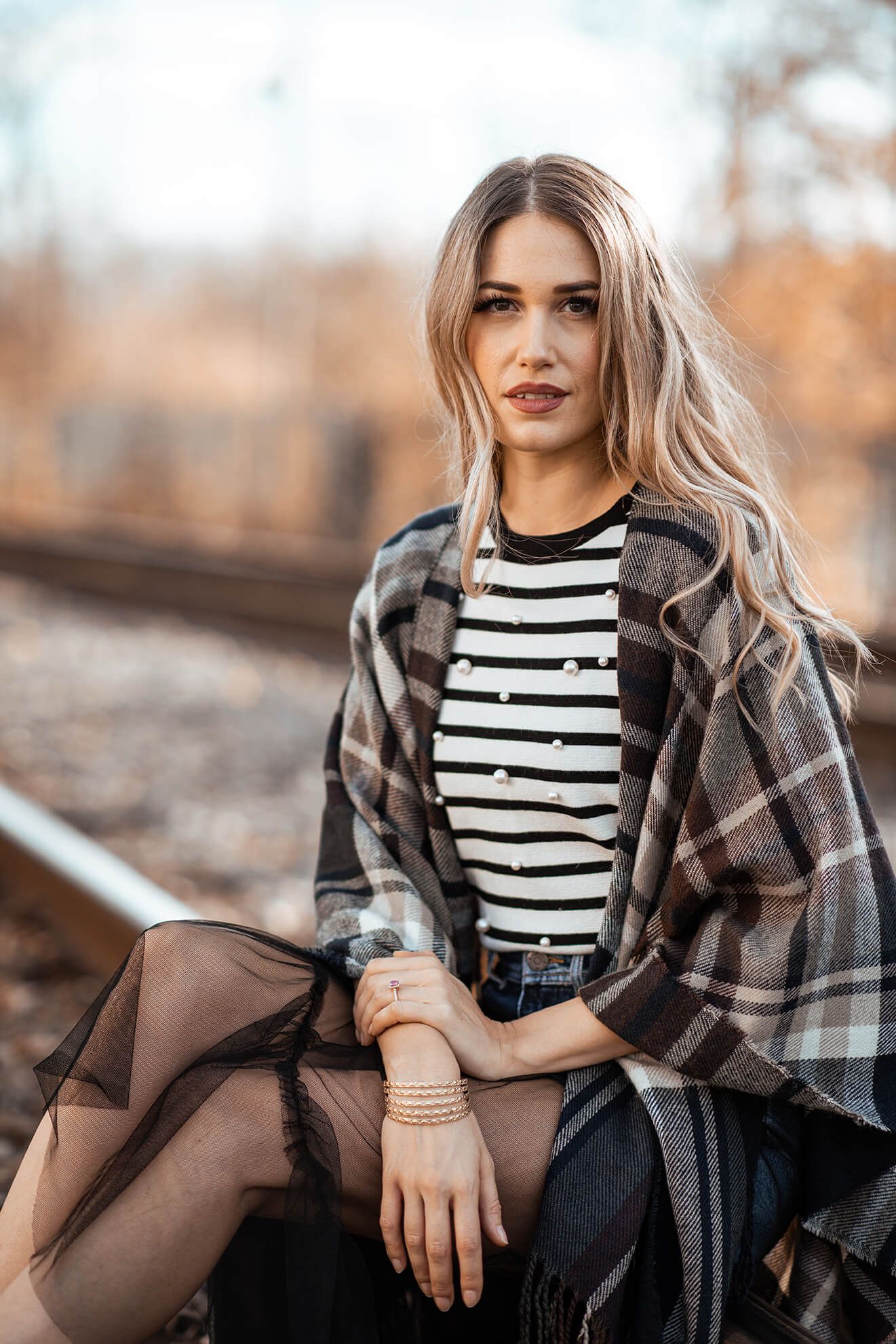 Fashion model wearing striped top and plaid shawl in autumn setting.