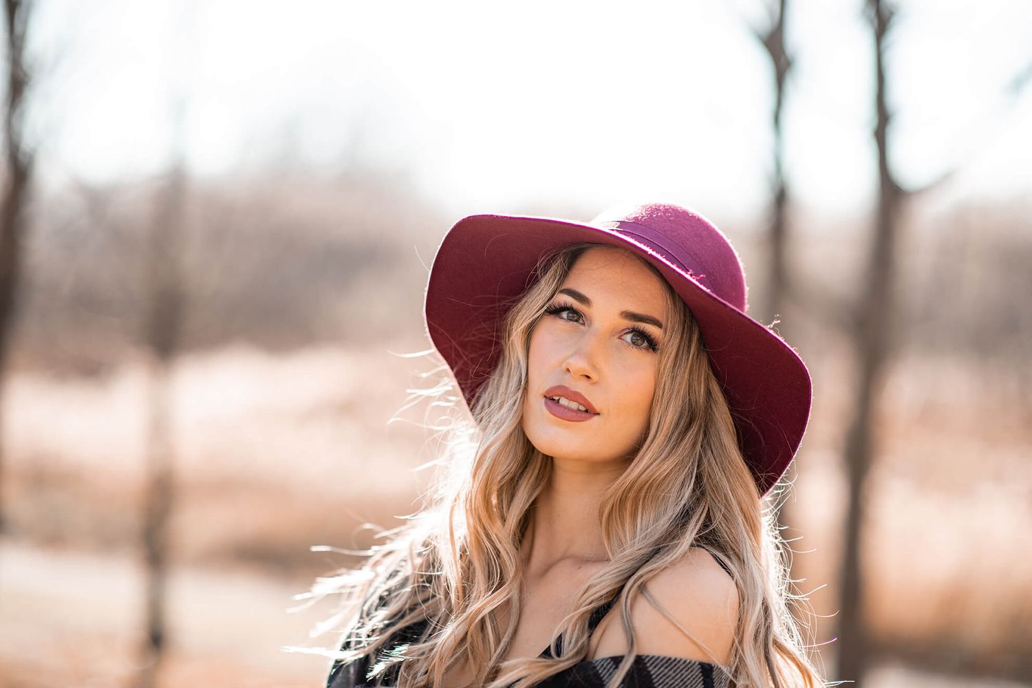 Stylish fall fashion portrait with burgundy hat and plaid shawl against autumn backdrop.