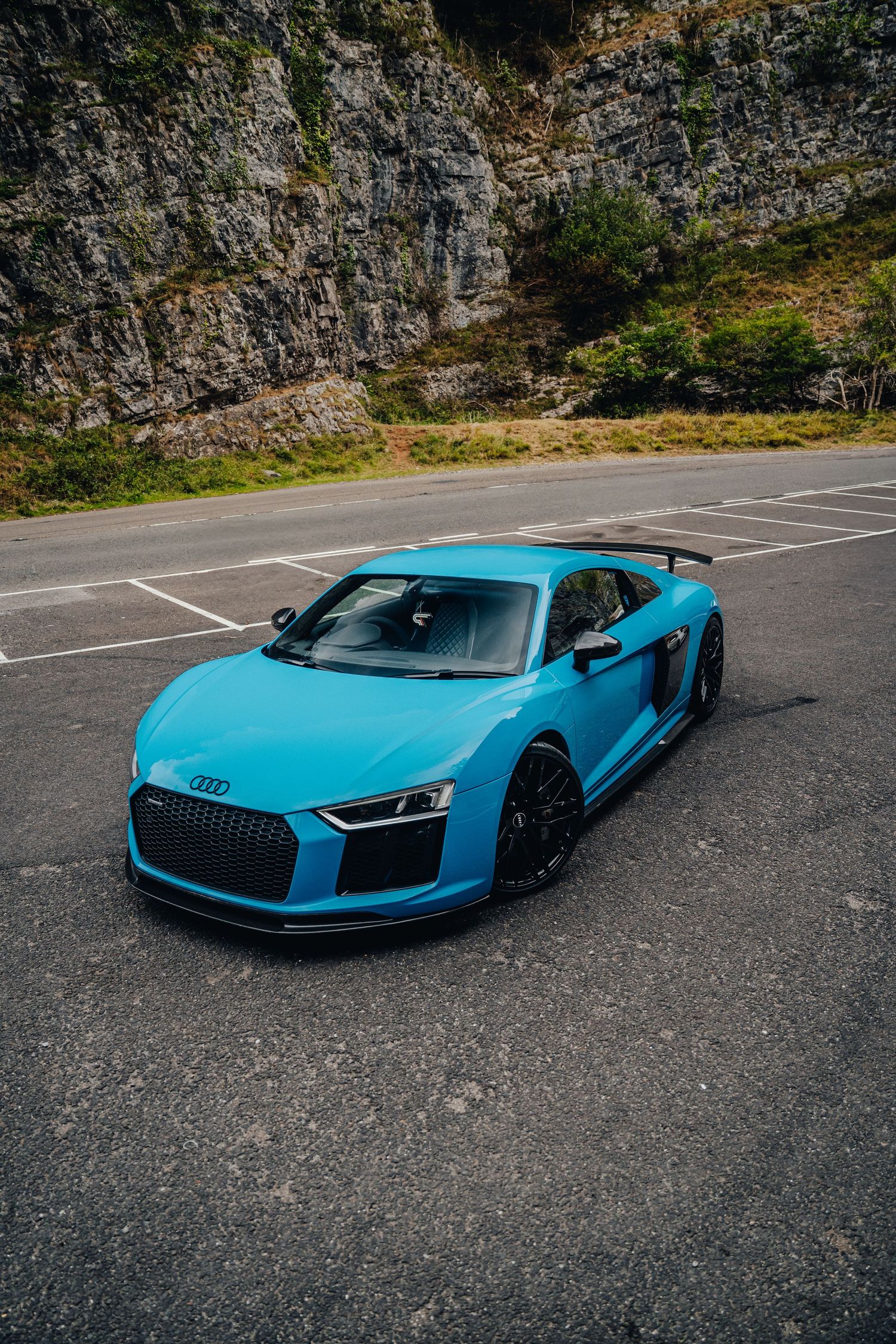 Multiple angles of a blue Audi R8 supercar parked in an empty lot with rock wall backdrop.
