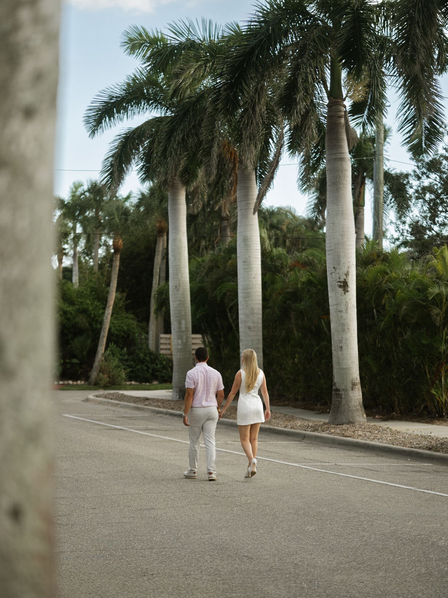 A couple strolls hand in hand down a palm tree-lined road in a tropical paradise.